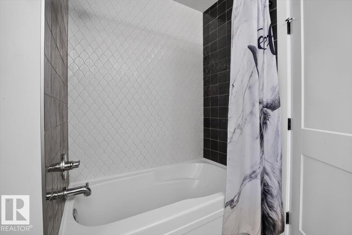 Bathtub with polished chrome fixtures, white scalloped tile surround, and contrasting dark tile accent wall - 94 Harvest Crescent, Ardrossan, AB - Indoor Photo Showing Bathroom