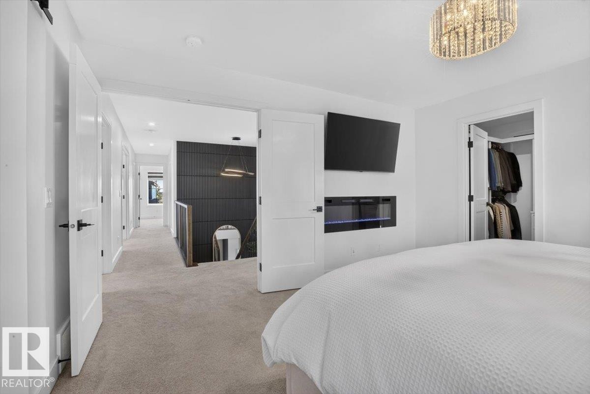 Integrated linear electric fireplace, modern crystal chandelier, walk-in closet, contemporary black accent wall, and wood railing - 94 Harvest Crescent, Ardrossan, AB - Indoor Photo Showing Bedroom