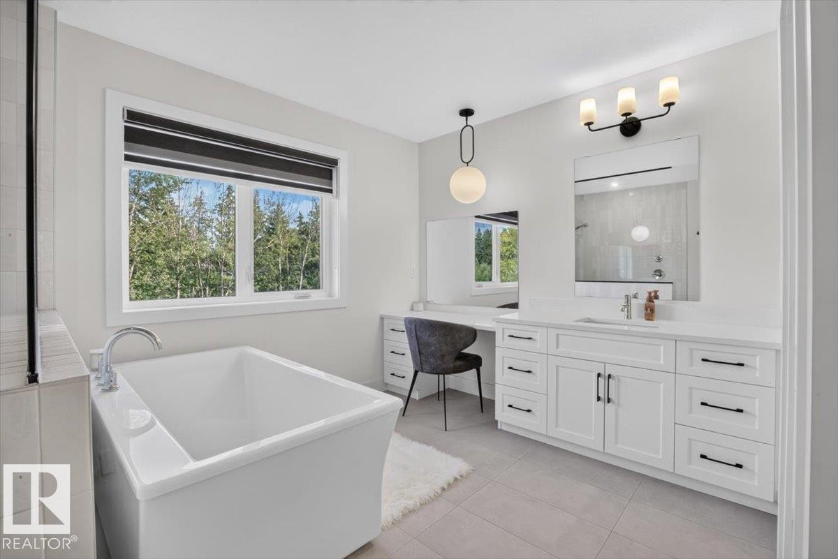 Freestanding soaking tub with polished chrome fixtures, expansive vanity with dual sinks, built-in makeup vanity, pendant lighting, and large format floor tiling - 94 Harvest Crescent, Ardrossan, AB - Indoor Photo Showing Bathroom