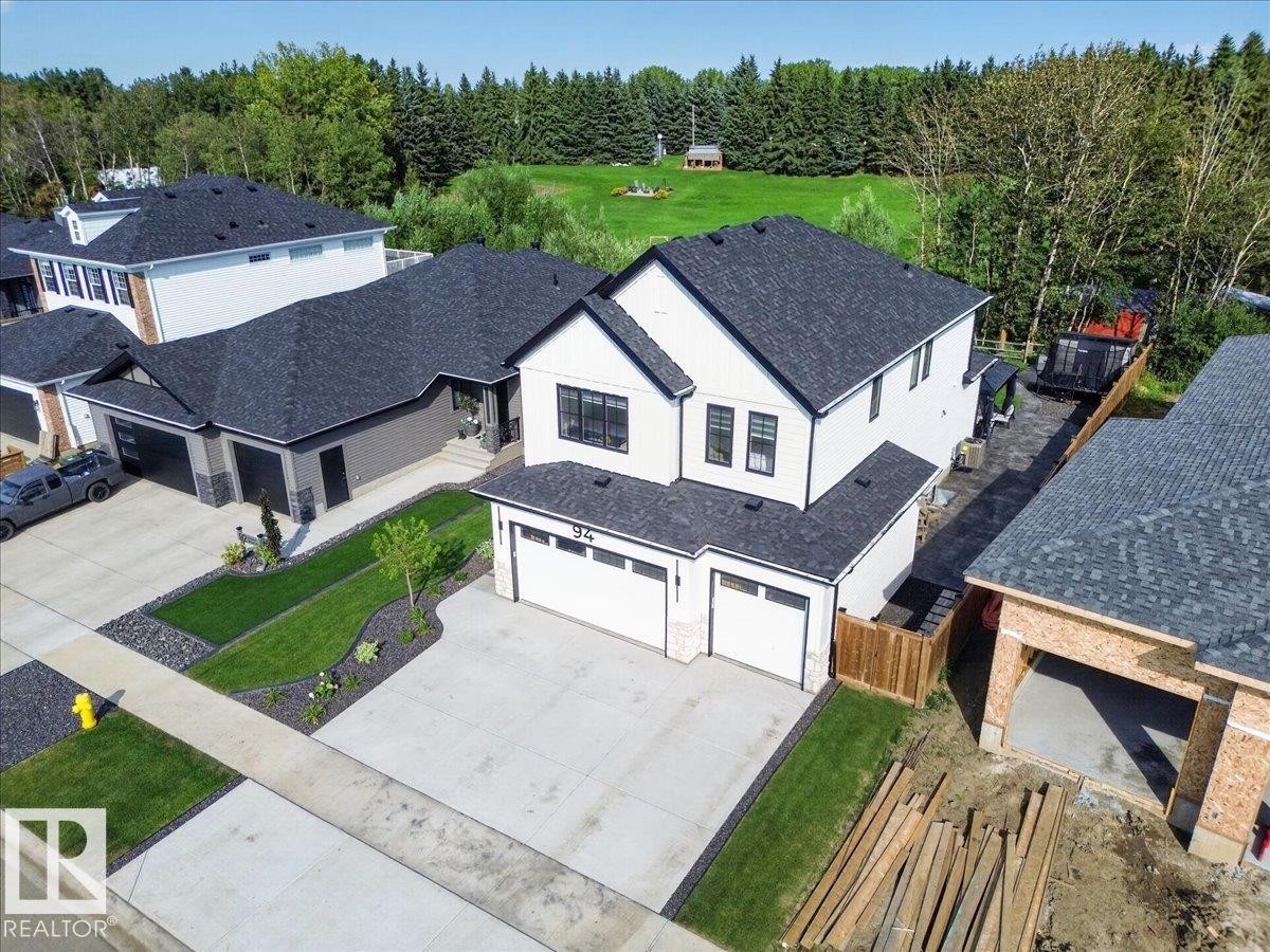 Newly constructed residence featuring a white and black exterior, black shingle roof, attached two-car garage, concrete driveway, and landscaped front yard - 94 Harvest Crescent, Ardrossan, AB - Outdoor