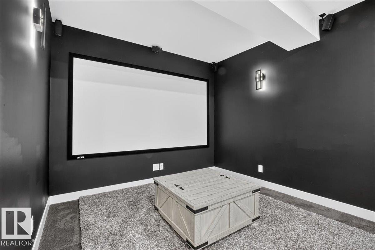 Media room featuring a large projection screen, dark wall finishes, wall sconces, ceiling-mounted speakers, and a carpeted floor - 94 Harvest Crescent, Ardrossan, AB - Indoor Photo Showing Other Room