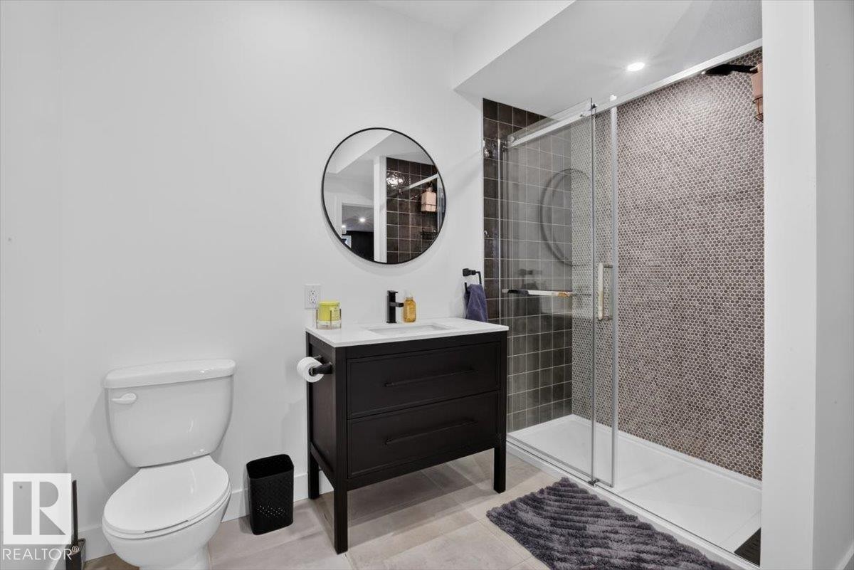 Black vanity with white countertop, round mirror, and glass-enclosed shower with mosaic tile - 94 Harvest Crescent, Ardrossan, AB - Indoor Photo Showing Bathroom