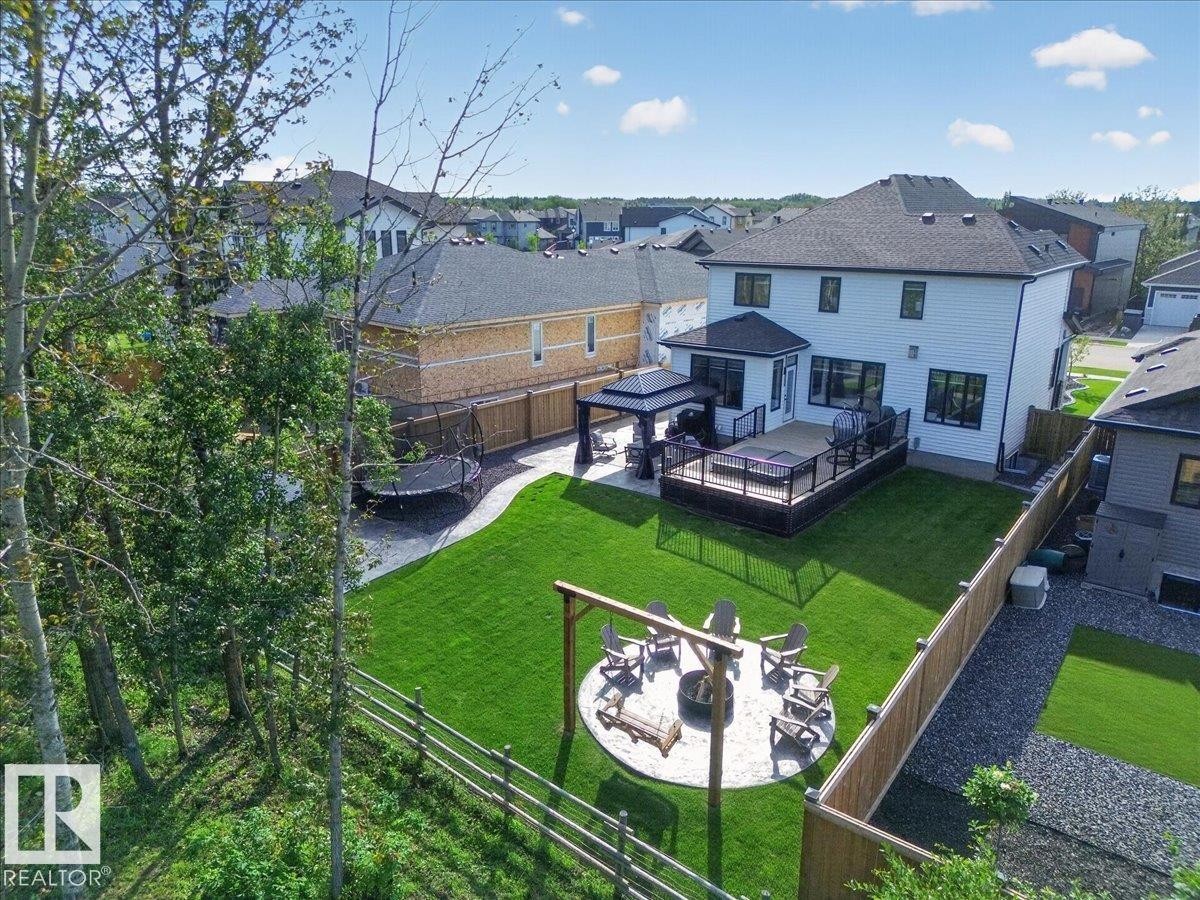 Expansive backyard with a manicured lawn, a gravel fire pit area, a multi-level deck, and a covered patio area - 94 Harvest Crescent, Ardrossan, AB - Outdoor With Deck Patio Veranda