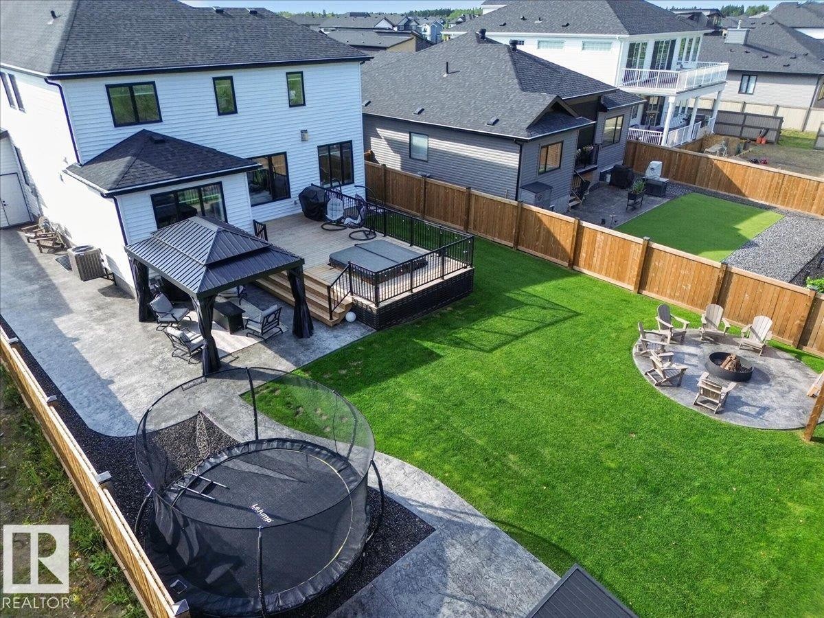 Expansive backyard featuring a manicured lawn, a large stamped concrete patio, a raised wood deck with a hot tub, a covered gazebo, and a circular fire pit area - 94 Harvest Crescent, Ardrossan, AB - Outdoor With Deck Patio Veranda With Exterior