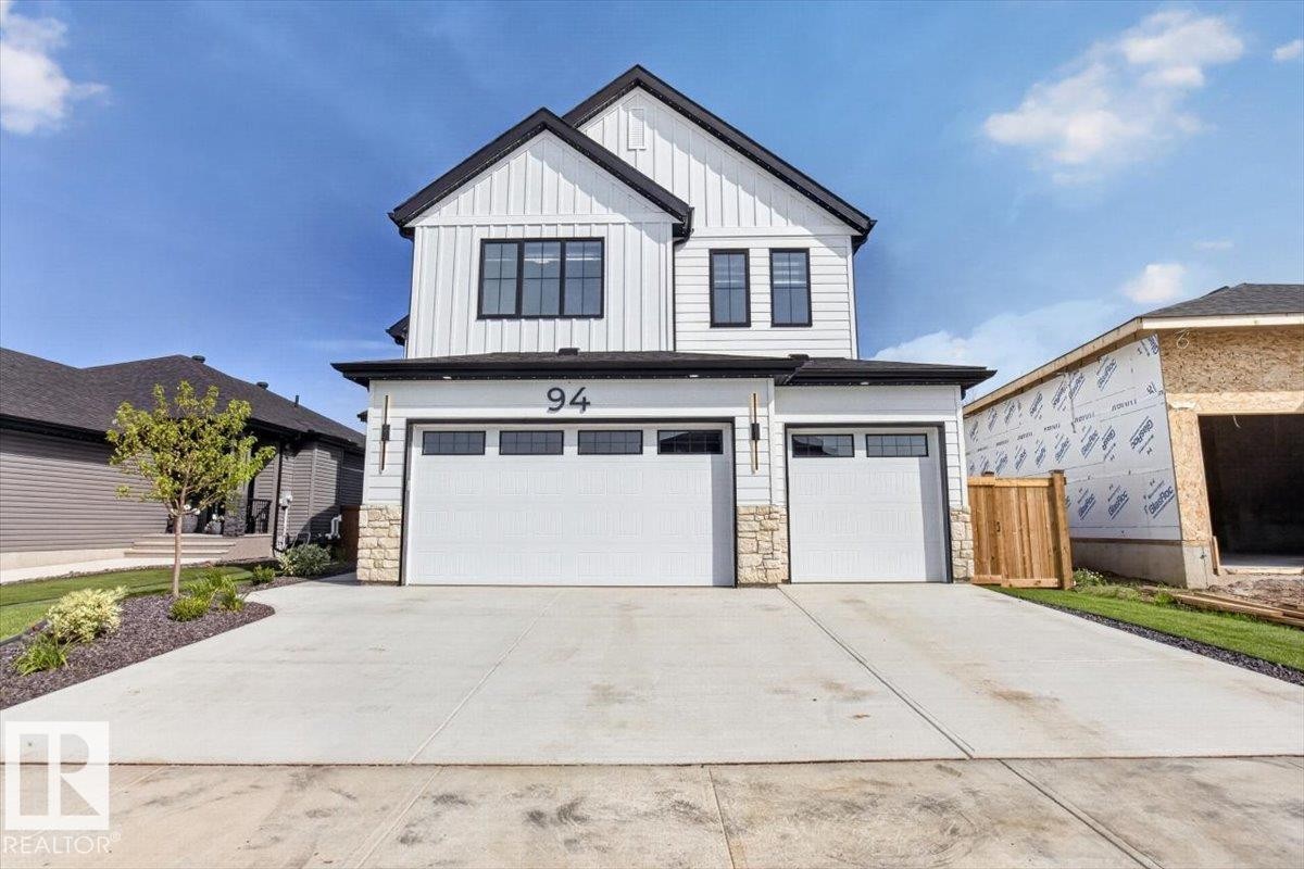 Two-story contemporary exterior with vertical white siding, black trim windows, and two garage doors - 94 Harvest Crescent, Ardrossan, AB - Outdoor