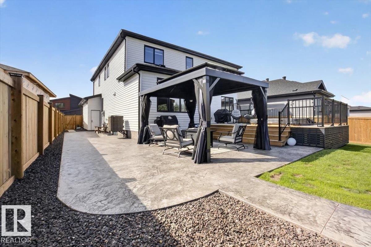 Stamped concrete patio, wooden privacy fence, elevated wooden deck with railing, detached shed, and a manicured lawn - 94 Harvest Crescent, Ardrossan, AB - Outdoor With Deck Patio Veranda With Exterior