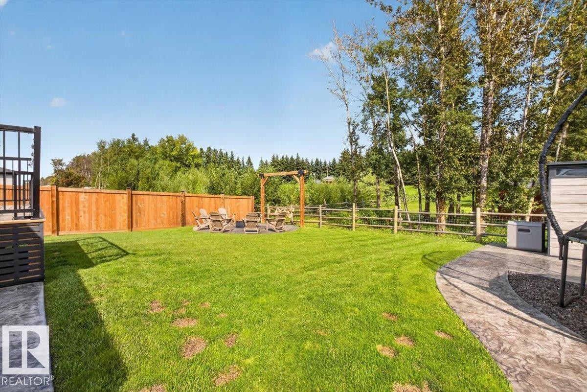 Expansive lawn area with a stamped concrete patio, wood privacy fencing, and a fire pit area with a wood pergola - 94 Harvest Crescent, Ardrossan, AB - Outdoor