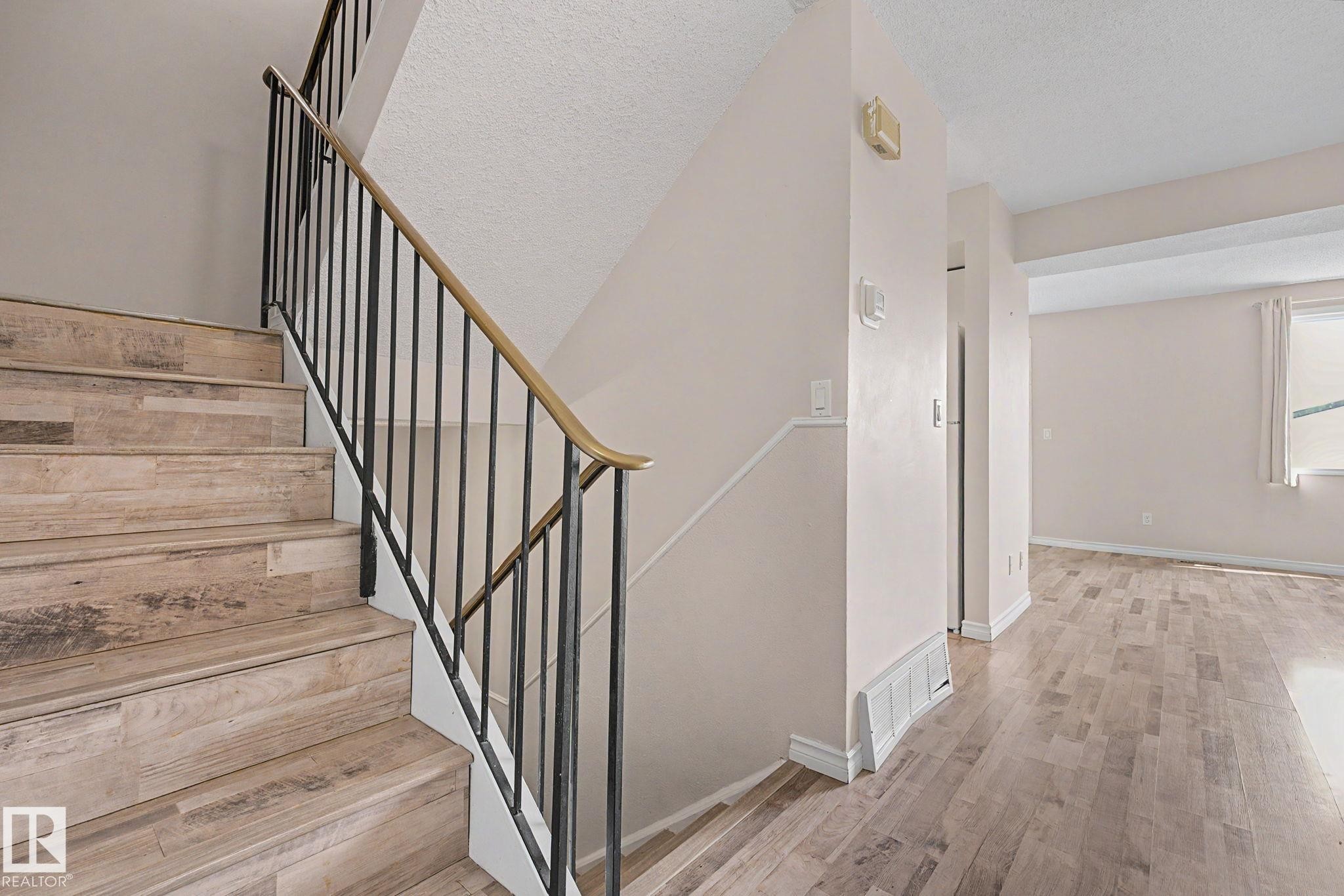 Staircase featuring wood-finish treads and risers, black metal balusters, and a brass-tone handrail - 1096 Knottwood Road Nw, Edmonton, AB - Indoor Photo Showing Other Room