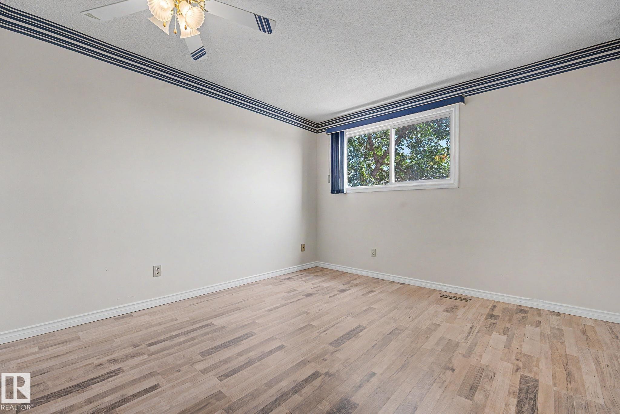 Spacious room featuring wood-finish flooring, a ceiling fan with integrated lighting, and a large window with blue blinds - 1096 Knottwood Road Nw, Edmonton, AB - Indoor Photo Showing Other Room
