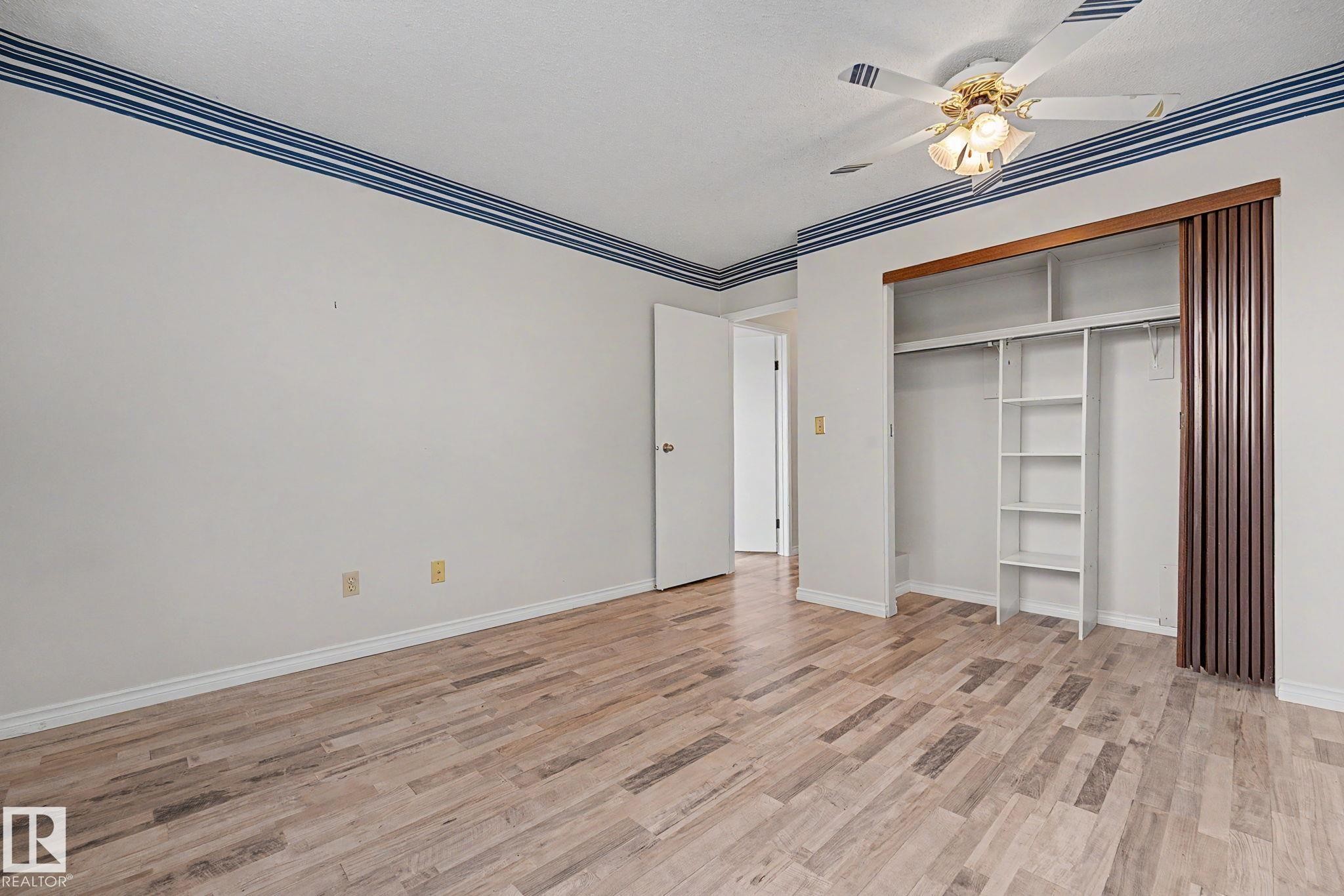 Spacious room featuring wood-finish flooring, a built-in closet with shelving and hanging rods, and a ceiling fan with integrated lighting - 1096 Knottwood Road Nw, Edmonton, AB - Indoor Photo Showing Other Room