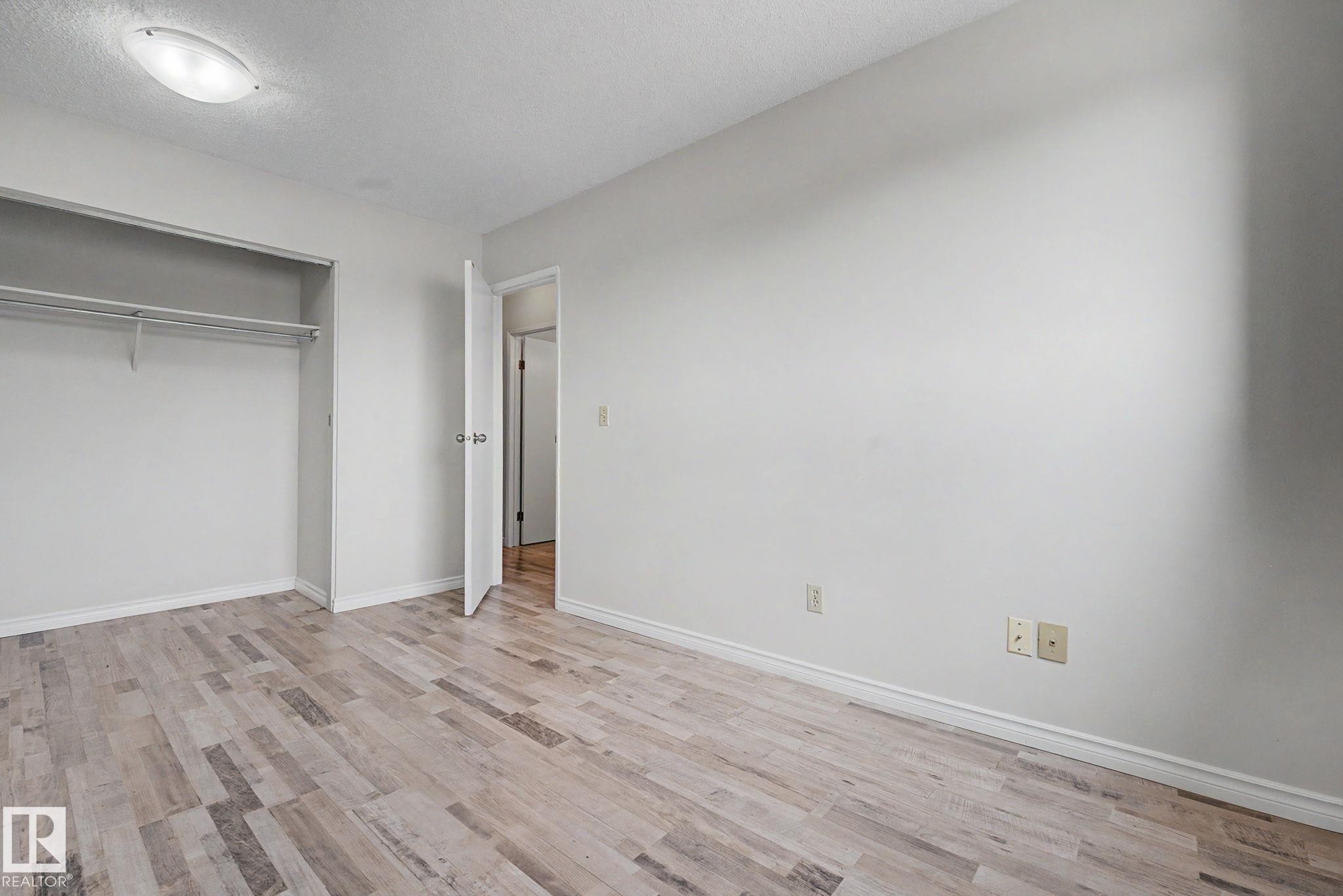 Spacious interior room featuring wood-finish flooring, white baseboards, and a built-in closet with shelving and hanging rod - 1096 Knottwood Road Nw, Edmonton, AB - Indoor Photo Showing Other Room