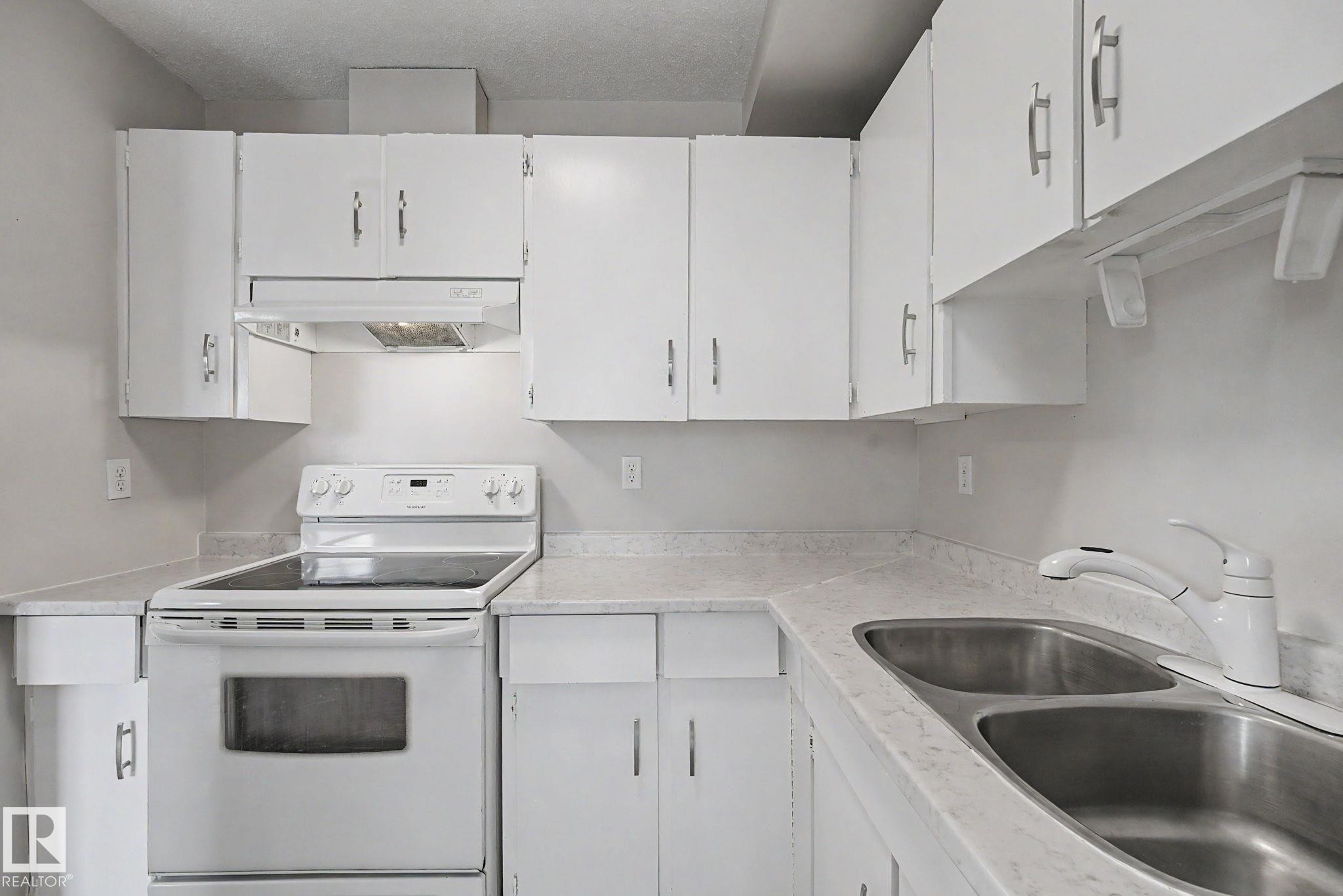 Bright kitchen featuring white cabinetry, a white electric range, and a double basin stainless steel sink with a white faucet - 1096 Knottwood Road Nw, Edmonton, AB - Indoor Photo Showing Kitchen With Double Sink