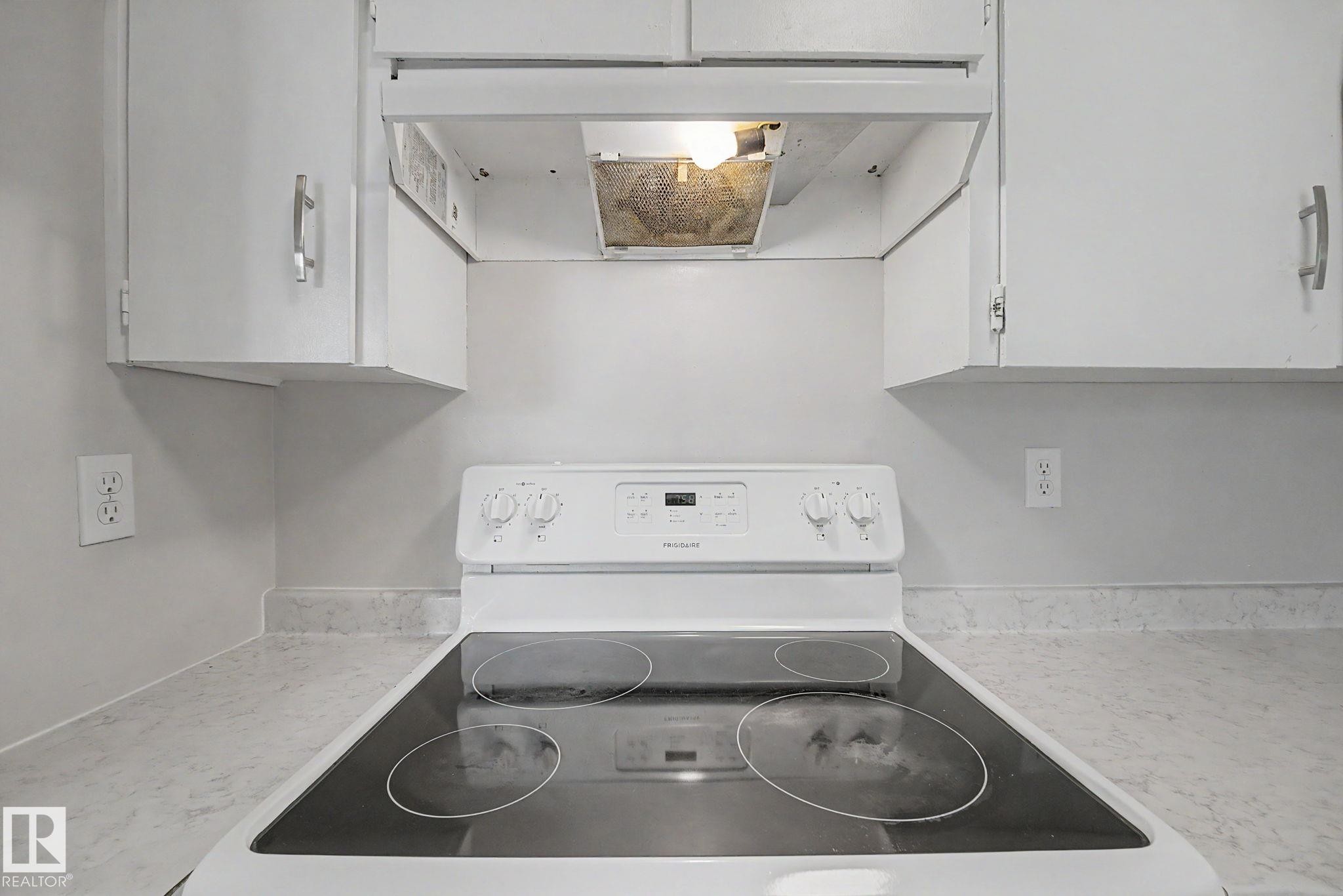 White electric range with a black smooth cooktop, complemented by white upper cabinetry with brushed nickel hardware, and stone-look countertops - 1096 Knottwood Road Nw, Edmonton, AB - Indoor Photo Showing Laundry Room