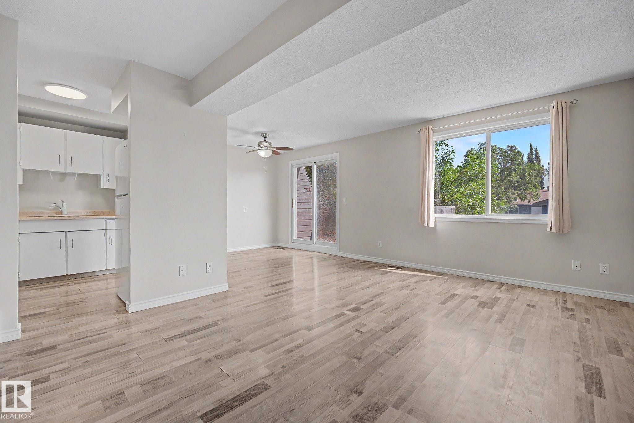 Spacious living area featuring wood-finish flooring, a ceiling fan, and a sliding glass door - 1096 Knottwood Road Nw, Edmonton, AB - Indoor