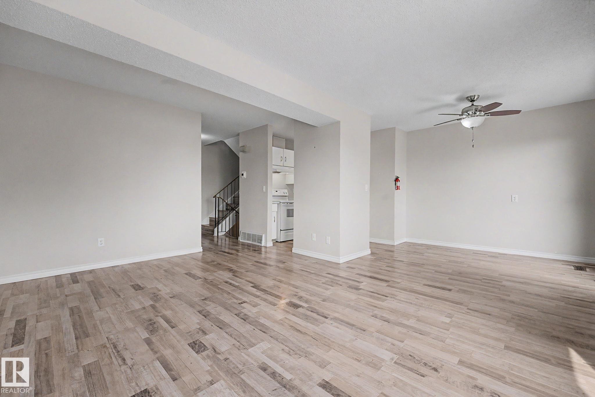 Spacious open-concept living area featuring wood-finish flooring, neutral wall tones, and a ceiling fan with integrated lighting - 1096 Knottwood Road Nw, Edmonton, AB - Indoor Photo Showing Other Room