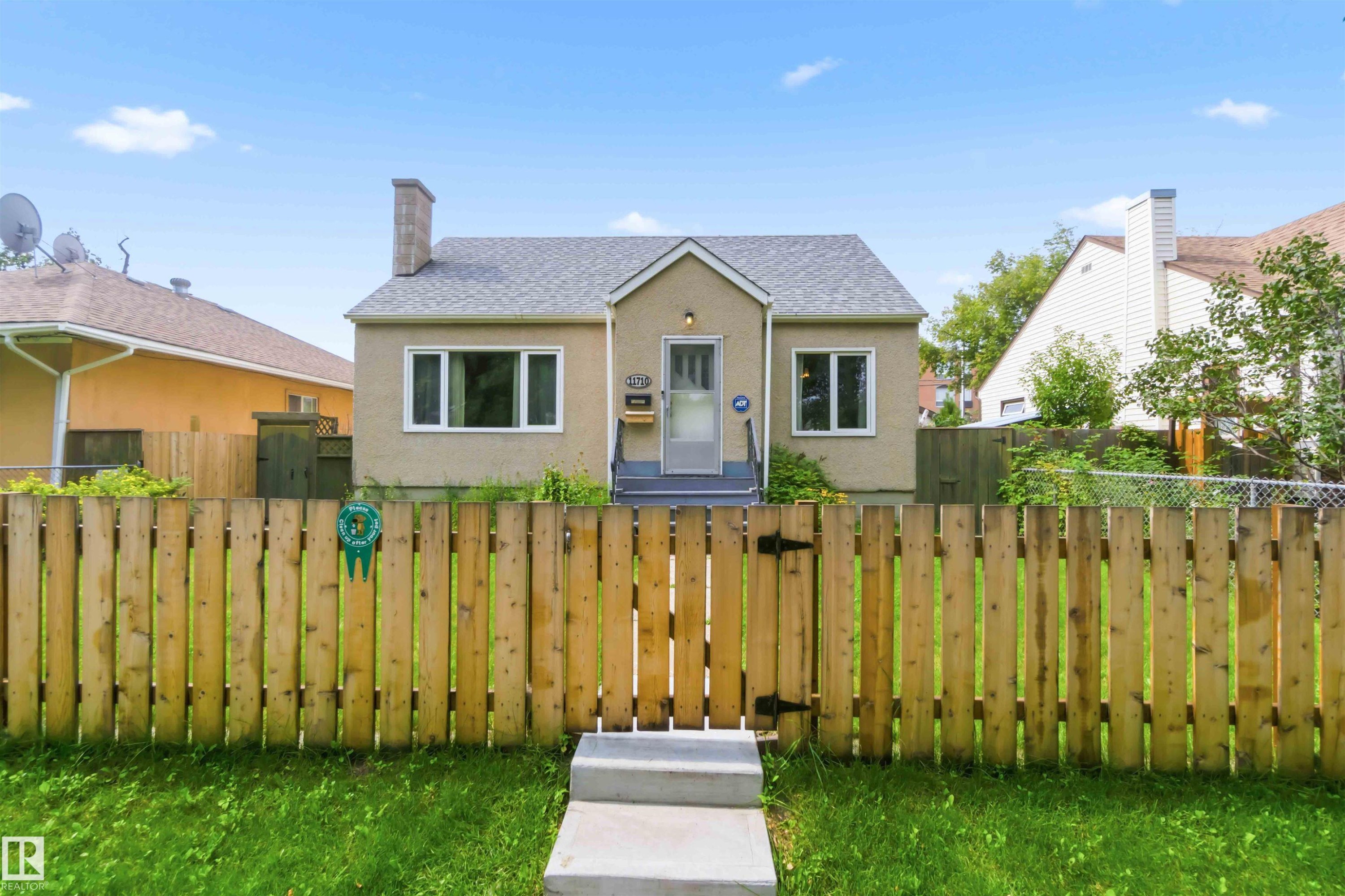 Stucco exterior, gabled roofline, front entry steps, front door with sidelight, and a wood privacy fence - 11710 94 Street Nw, Edmonton, AB - Outdoor