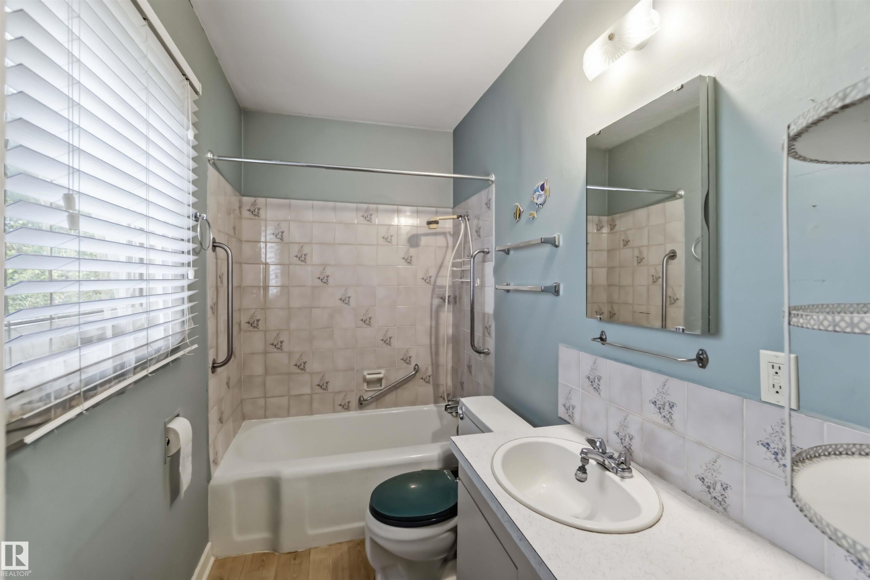 Bathtub shower combination with tiled surround, single vanity with integrated sink, and wood-finish flooring - 11710 94 Street Nw, Edmonton, AB - Indoor Photo Showing Other Room