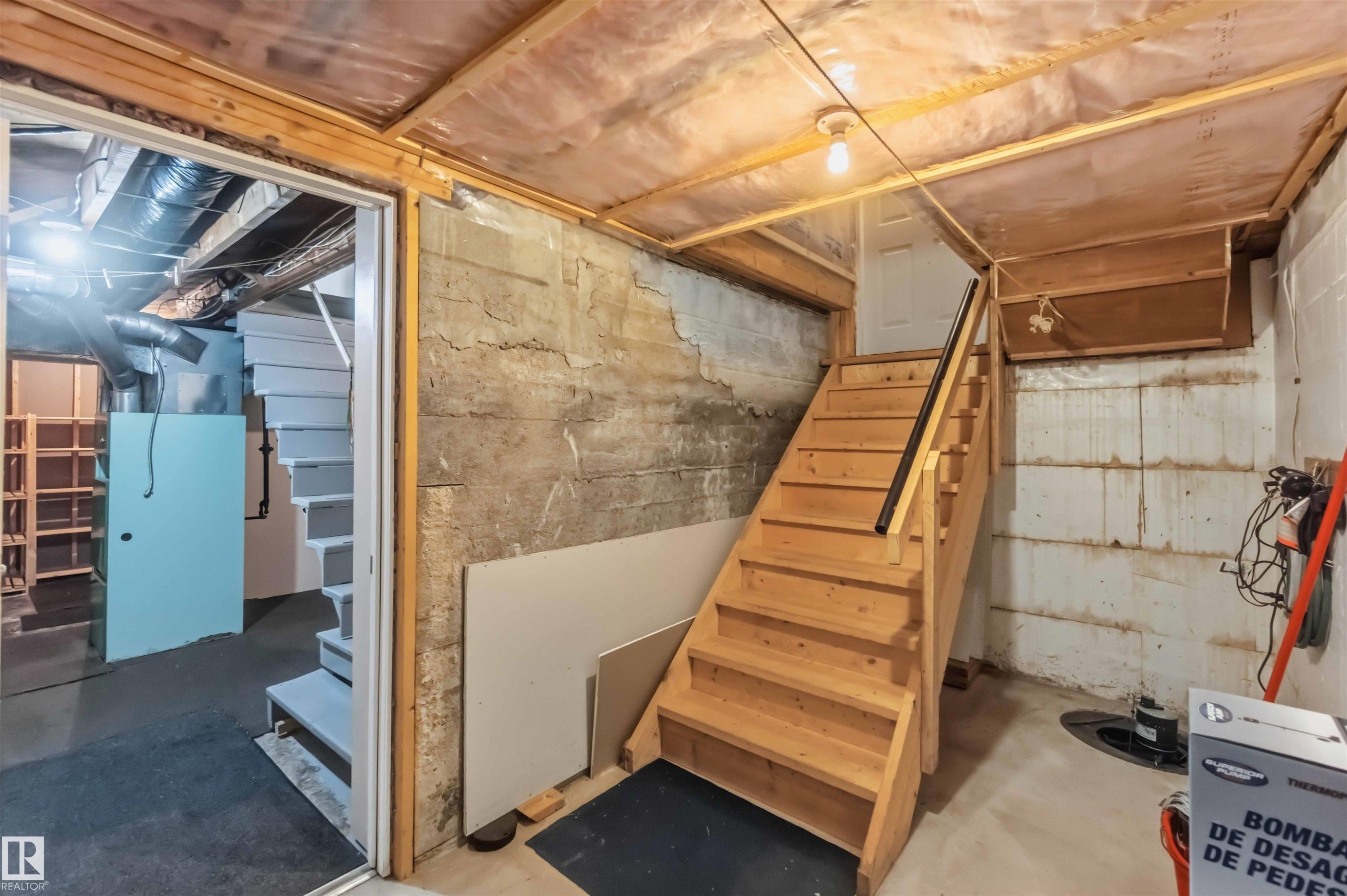 Unfinished basement with exposed concrete walls, wood-framed ceiling, and a wooden staircase with a black handrail - 11710 94 Street Nw, Edmonton, AB - Indoor