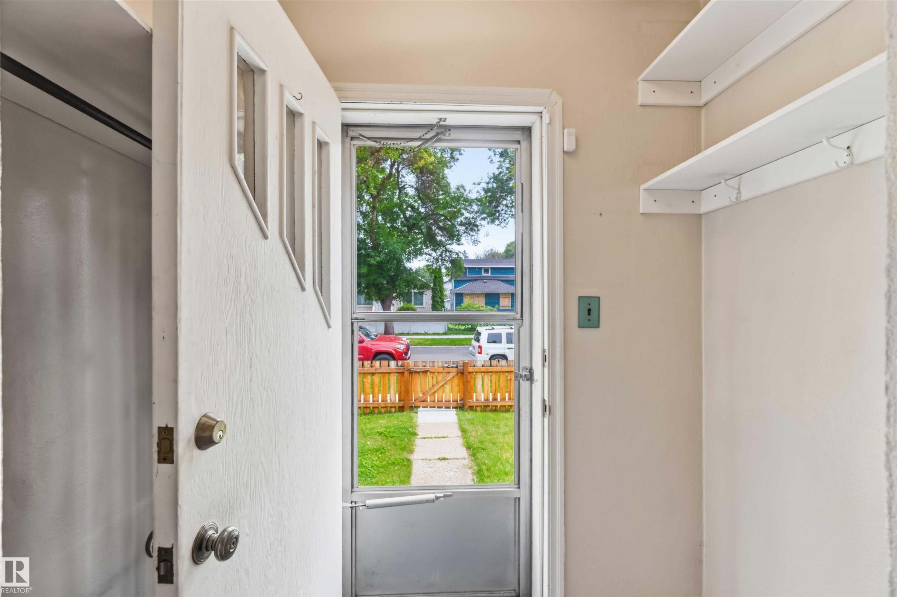 Entryway with a solid white door featuring three upper panels, a screen door, and two white floating shelves - 11710 94 Street Nw, Edmonton, AB - Outdoor