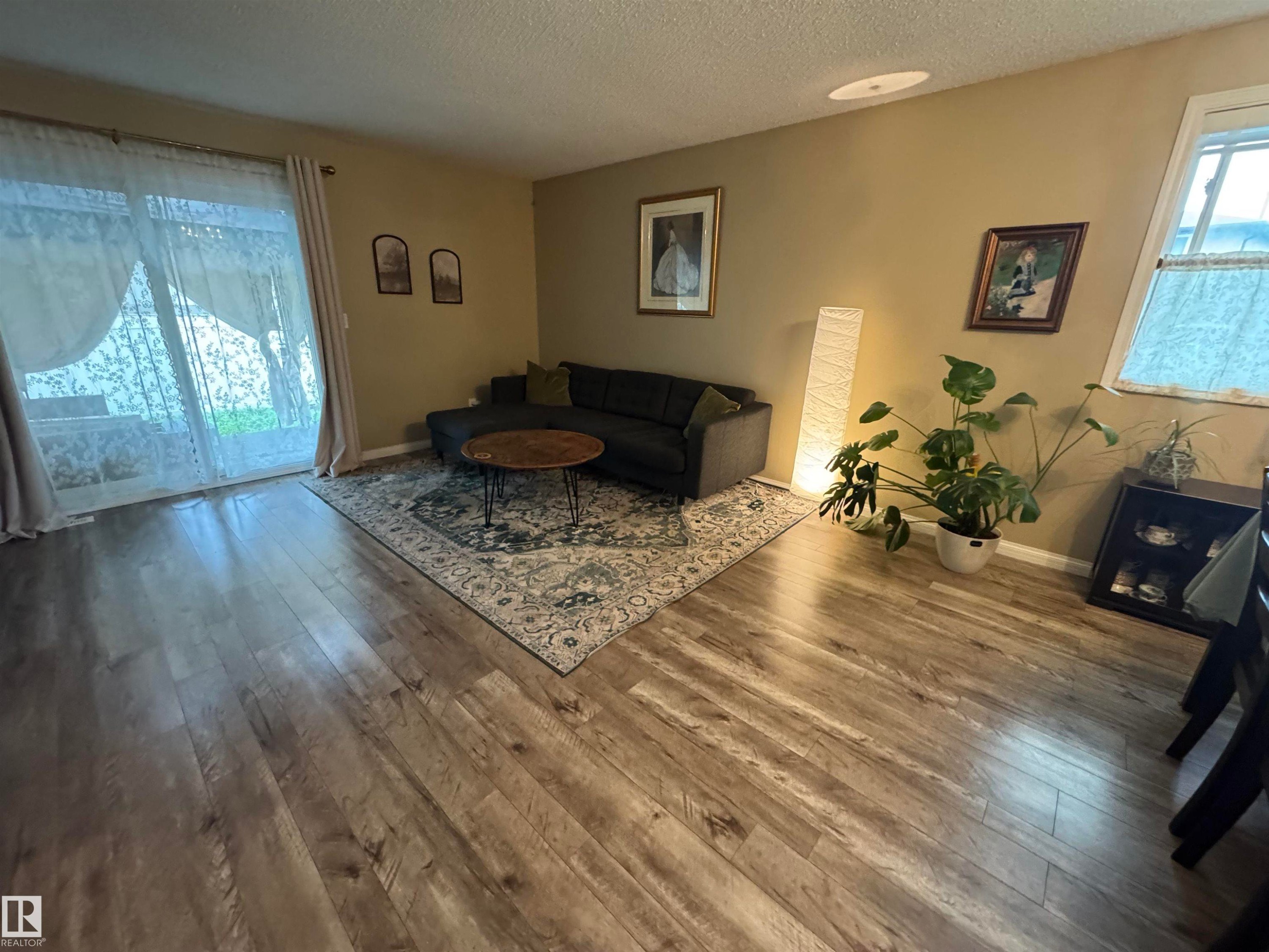 Wood-finish flooring throughout, complemented by warm-toned wall finishes and a sliding glass door - #38 8930 99 Av, Fort Saskatchewan, AB