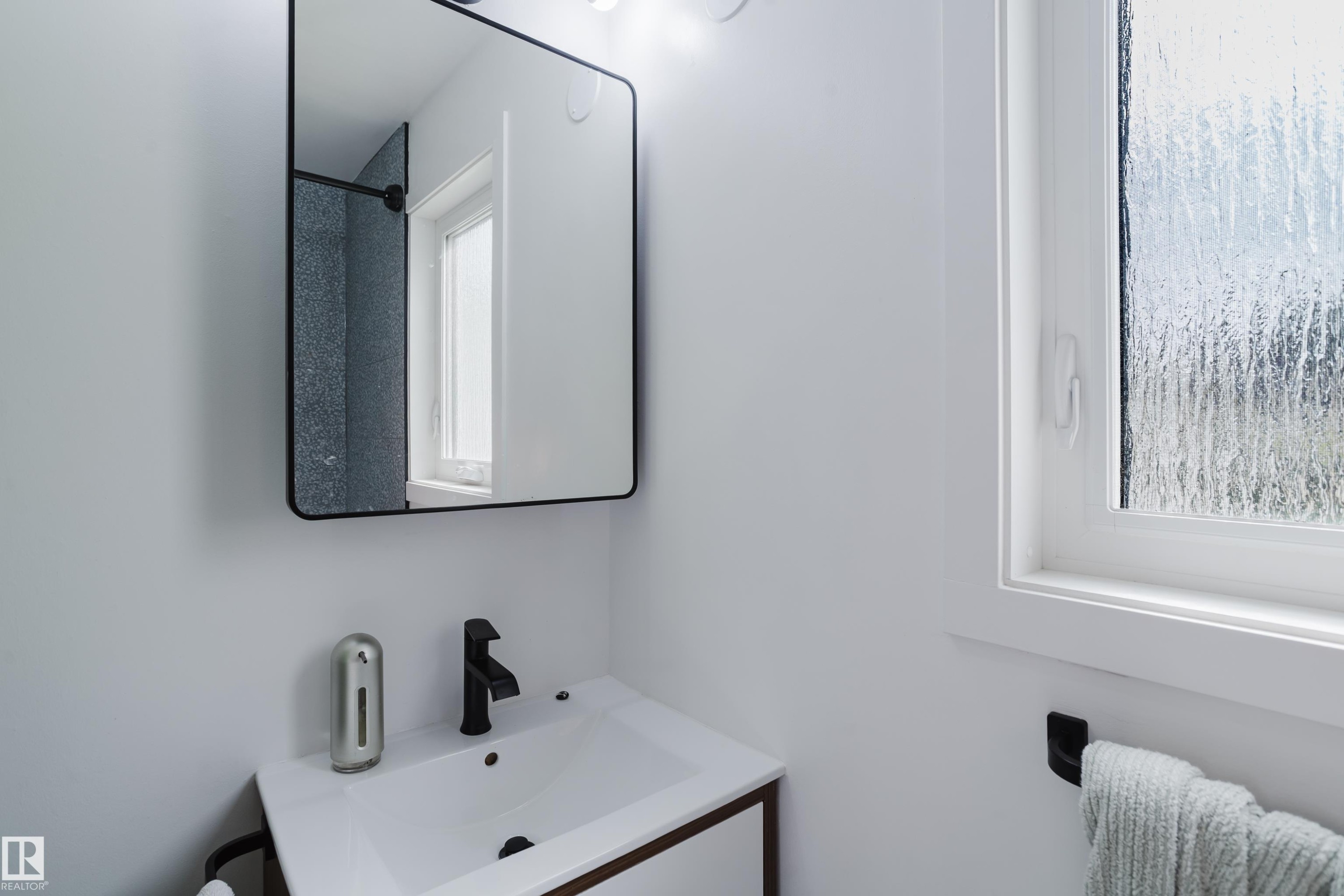 White vanity with a rectangular sink, matte black faucet, and a rectangular mirror with a black frame - 9059 52 Street Nw, Edmonton, AB - Indoor Photo Showing Bathroom