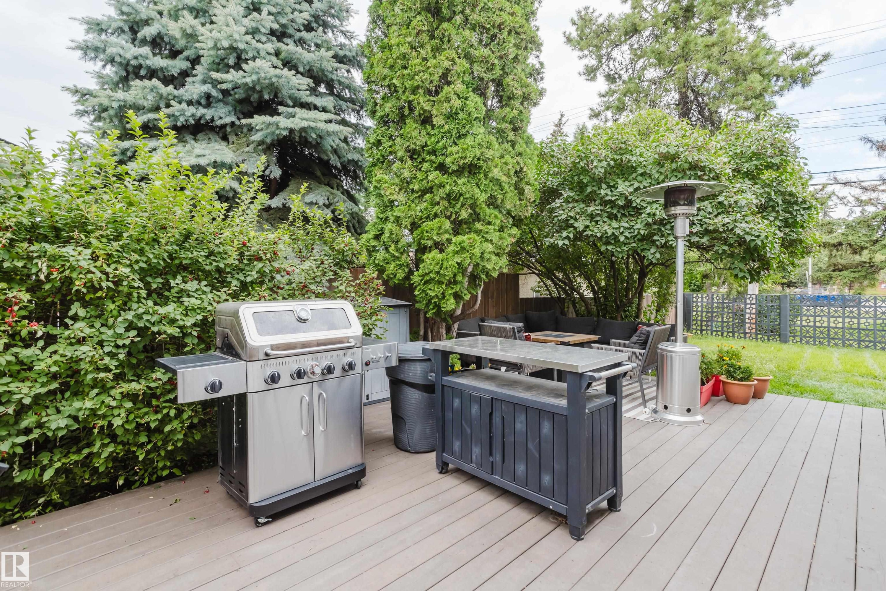 Expansive outdoor deck with composite decking, surrounded by mature trees and shrubs, featuring a built-in outdoor bar - 9059 52 Street Nw, Edmonton, AB - Outdoor With Deck Patio Veranda With Exterior