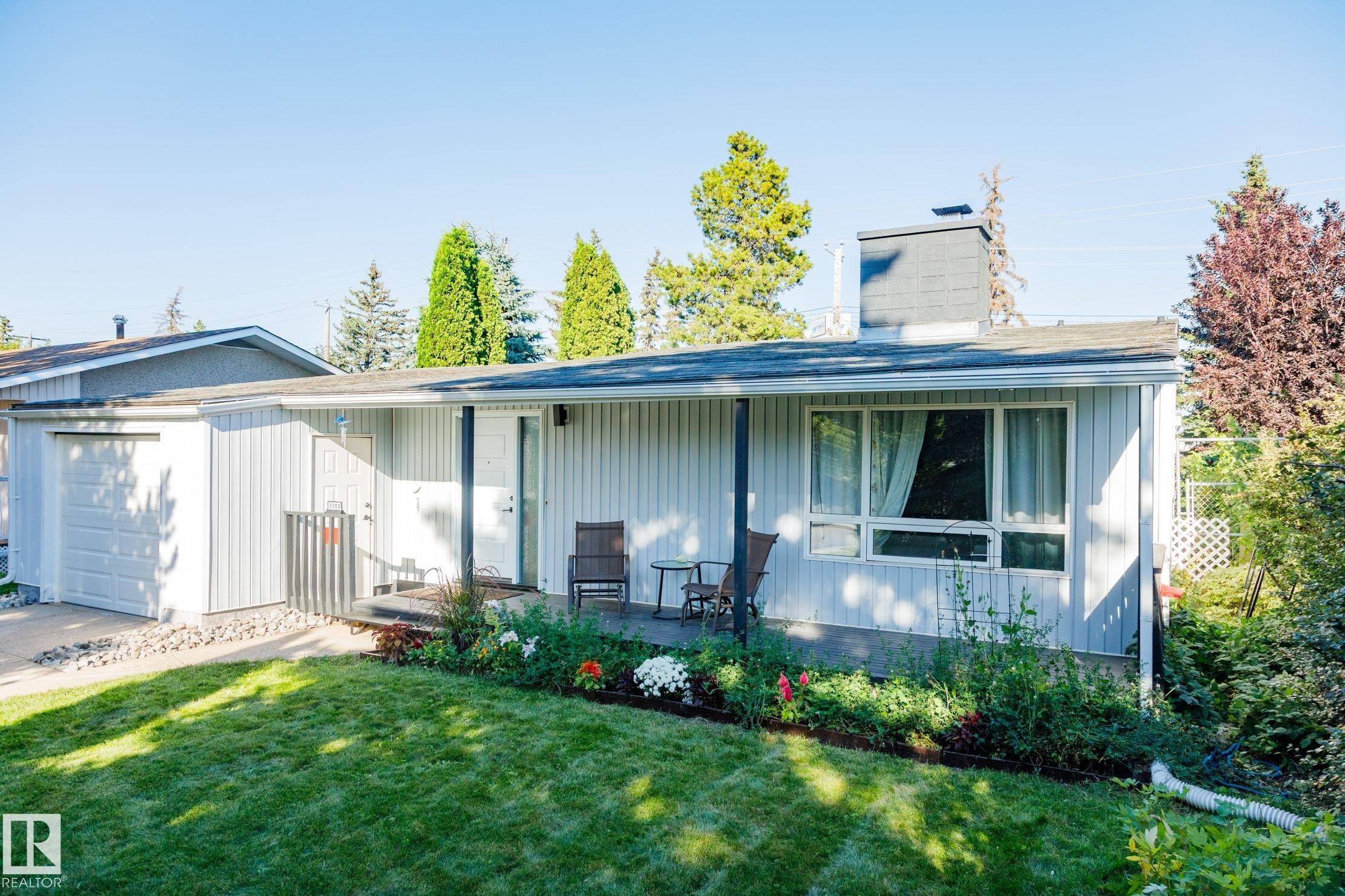 Modern single-story residence featuring corrugated metal siding, a covered front porch with large windows, and an attached garage - 9059 52 Street Nw, Edmonton, AB - Outdoor With Deck Patio Veranda