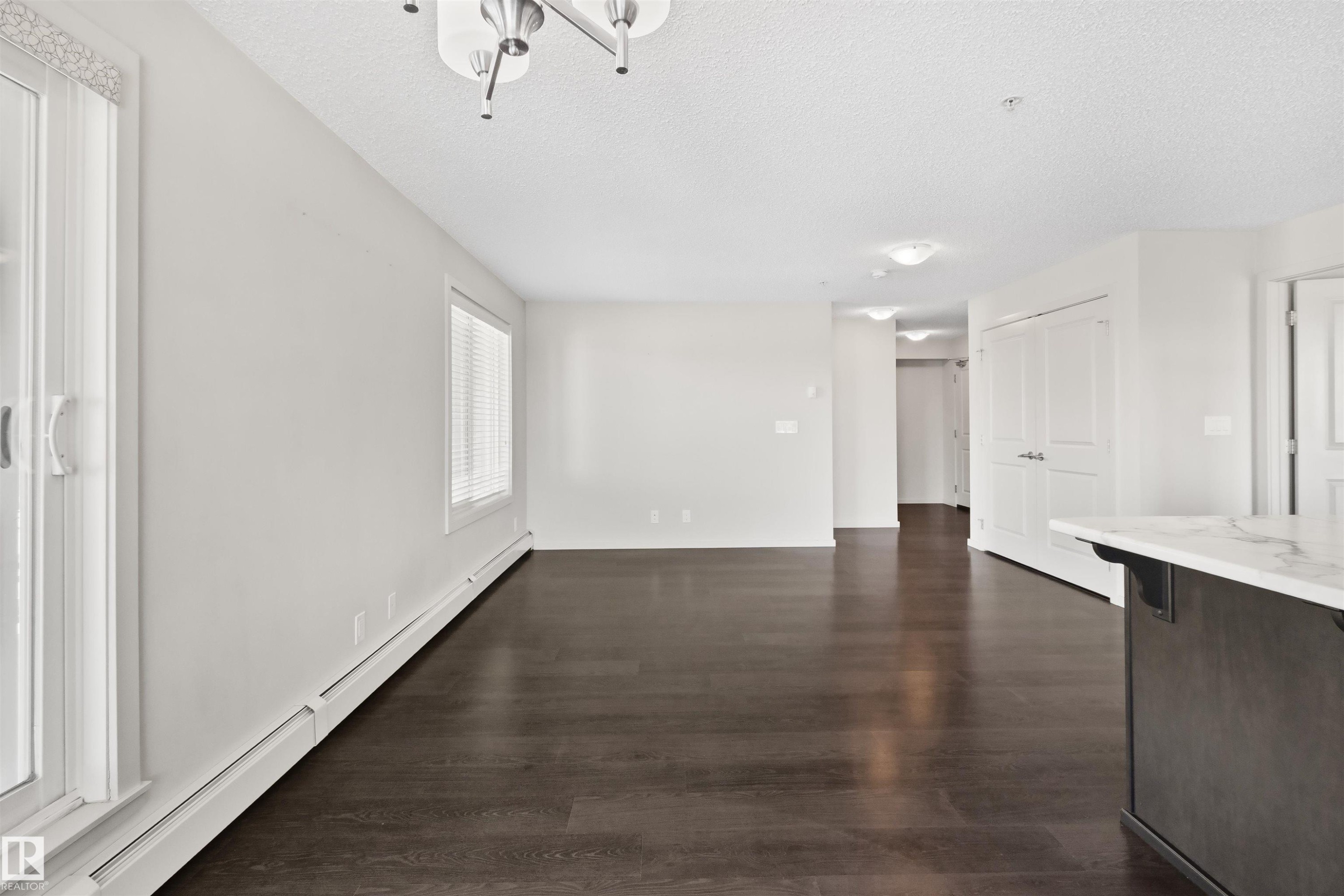 Spacious open-concept room featuring dark wood-finish flooring, white walls, and multiple windows - #318 5521 7 Av Sw Sw, Edmonton, AB - Indoor Photo Showing Other Room