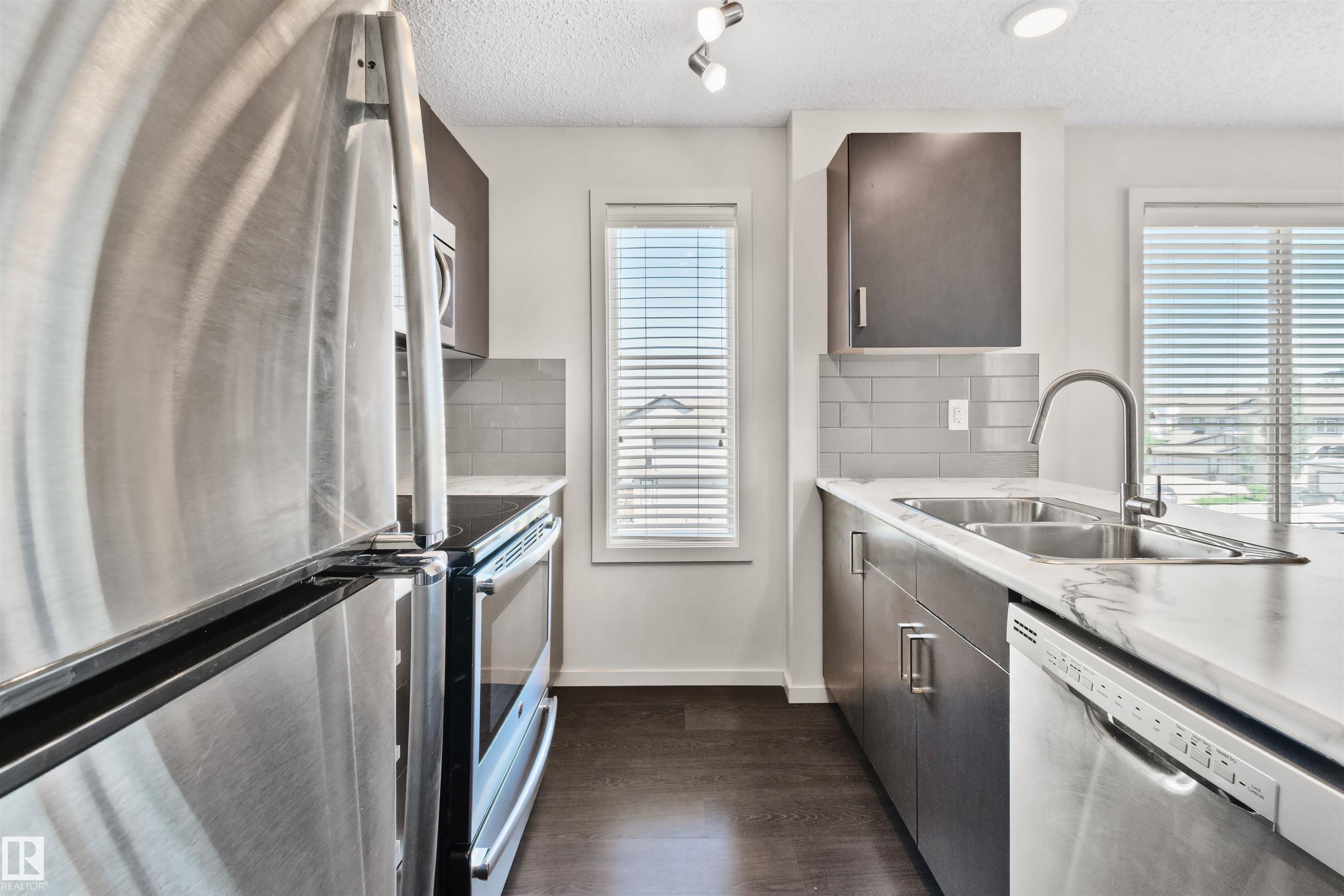 Stainless steel appliances, dark wood-finish cabinetry, light marble-look countertops, subway tile backsplash, and dark wood-finish flooring - #318 5521 7 Av Sw Sw, Edmonton, AB - Indoor Photo Showing Kitchen With Stainless Steel Kitchen With Double Sink With Upgraded Kitchen