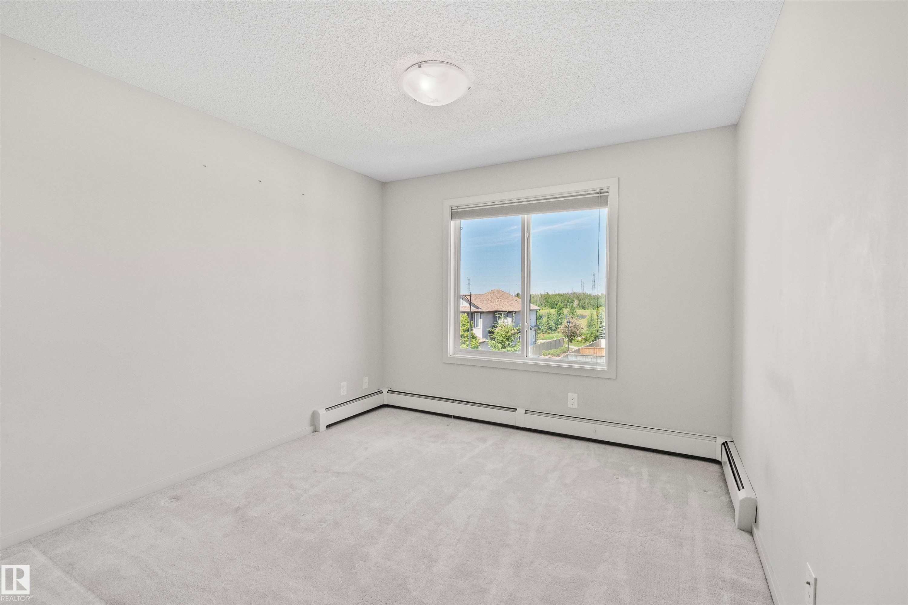 Light gray wall finishes with a window providing exterior scenery, accompanied by light gray carpet flooring - #318 5521 7 Av Sw Sw, Edmonton, AB - Indoor Photo Showing Other Room