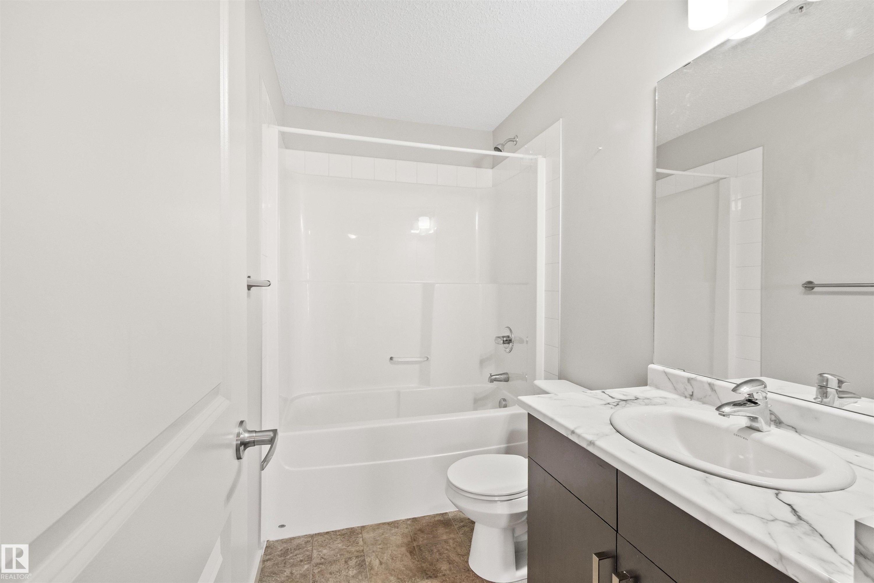 Bathroom featuring a white bathtub, shower with glass enclosure, single vanity with oval sink, stone-finish countertop, and dark wood-finish cabinetry - #318 5521 7 Av Sw Sw, Edmonton, AB - Indoor Photo Showing Bathroom
