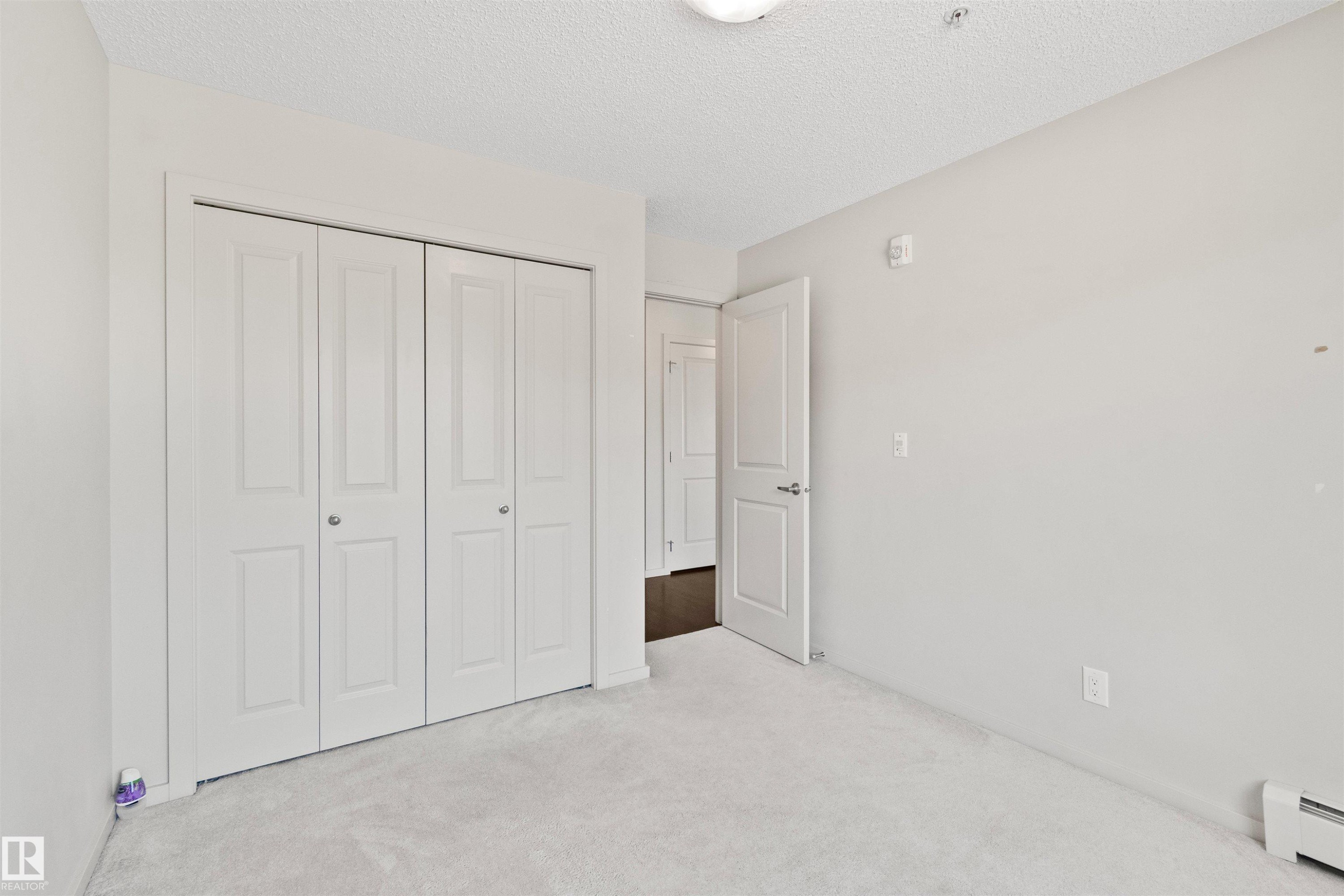 Neutral wall paint, carpeted flooring, bi-fold closet doors, and interior paneled door - #318 5521 7 Av Sw Sw, Edmonton, AB - Indoor