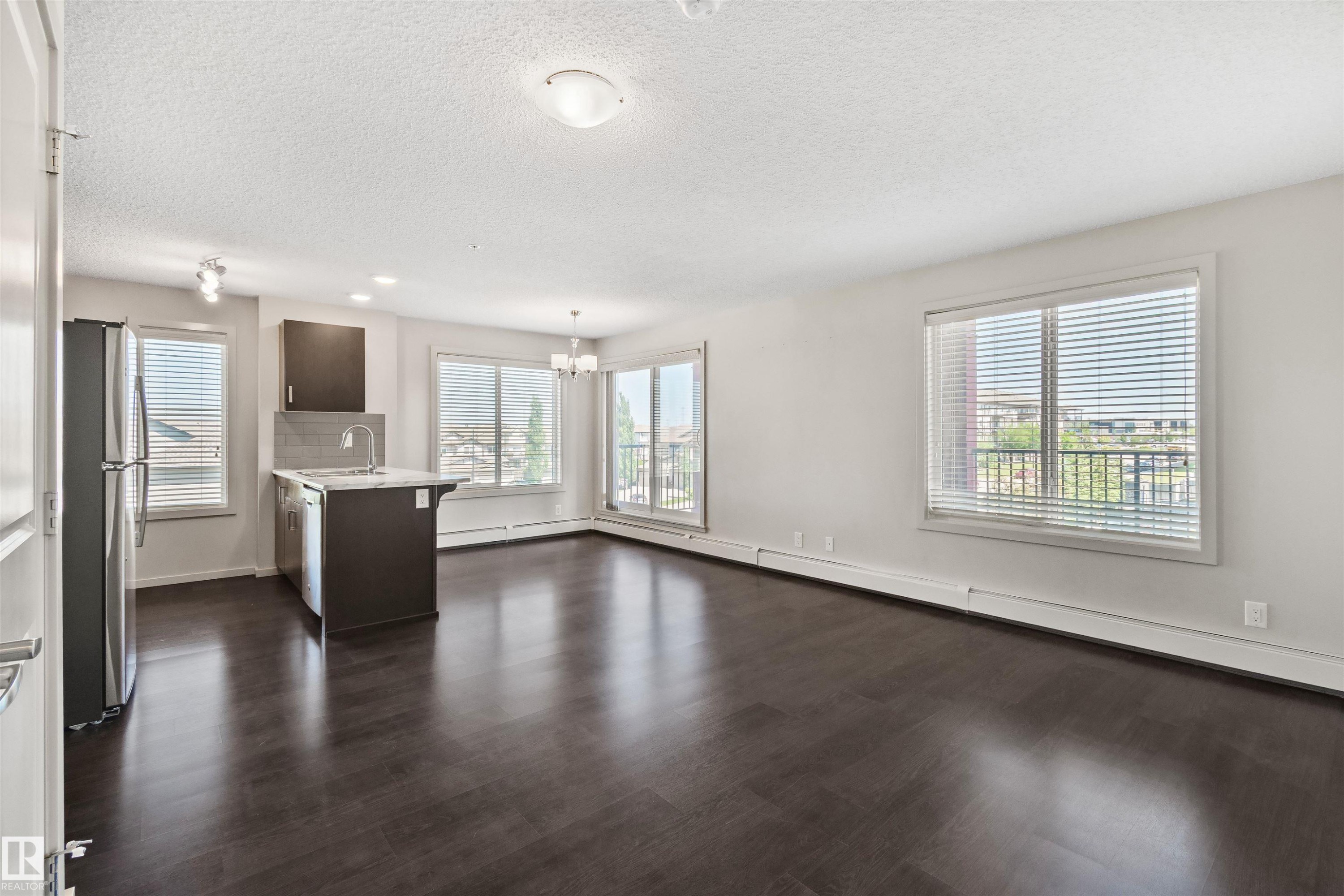 Open-concept living space with dark wood-finish flooring, white walls, and multiple windows - #318 5521 7 Av Sw Sw, Edmonton, AB - Indoor Photo Showing Kitchen