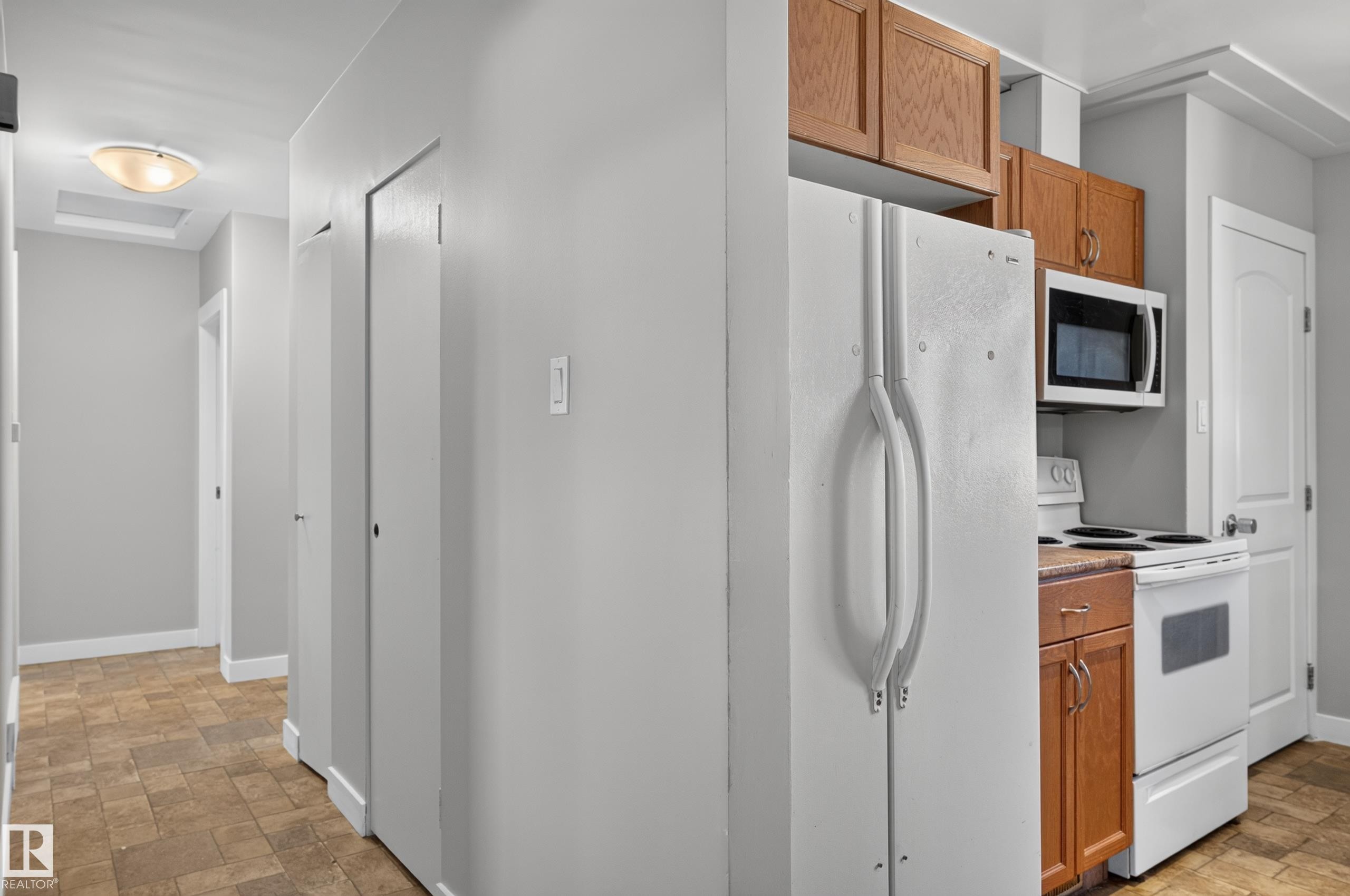 Kitchenette area featuring wood cabinetry, white appliances, and a built-in microwave - 13214 123 Street Nw, Edmonton, AB