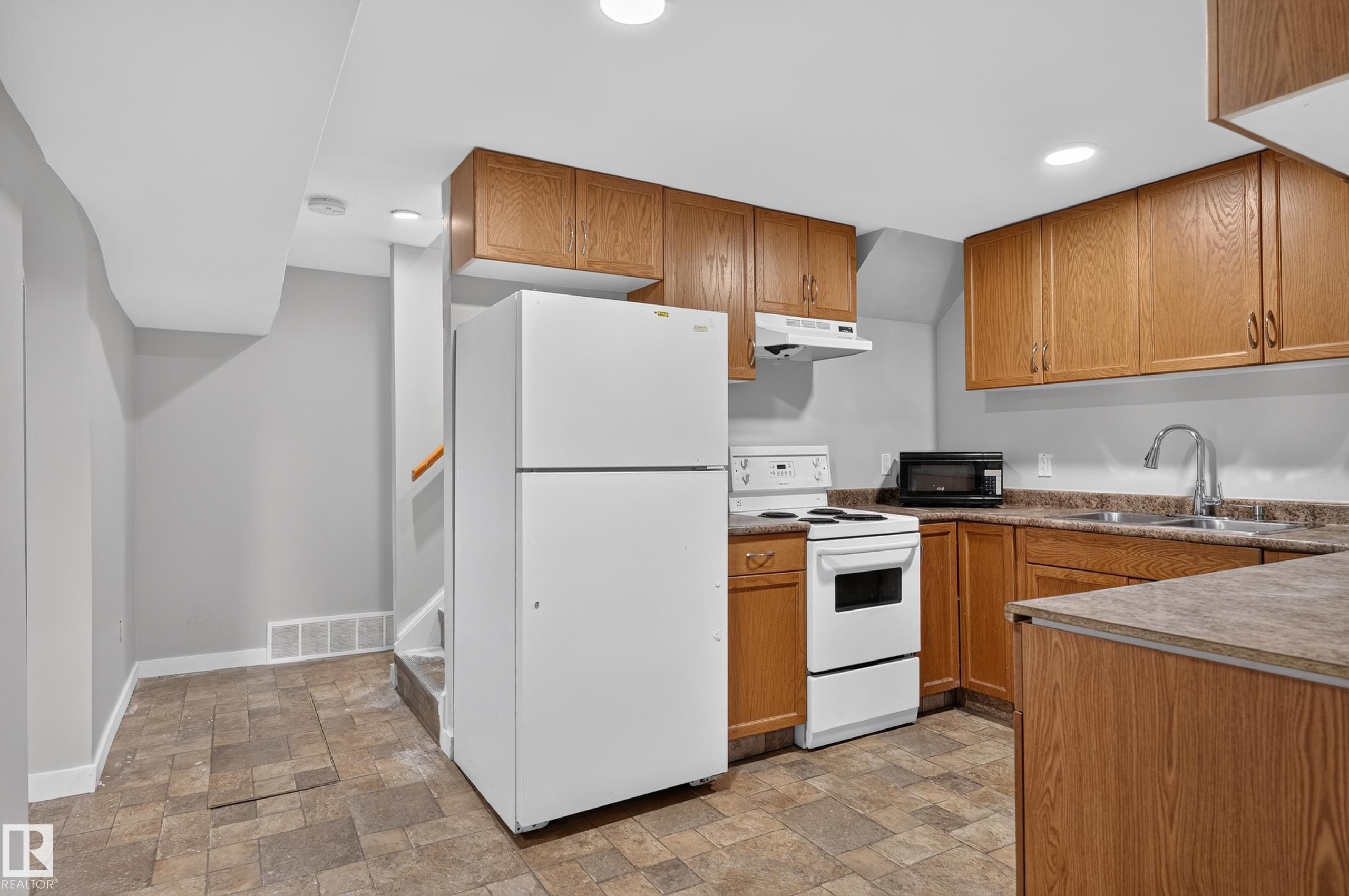 Full kitchen featuring wood-finish cabinetry, a freestanding electric range, and a stainless-steel sink with a gooseneck faucet - 13214 123 Street Nw, Edmonton, AB