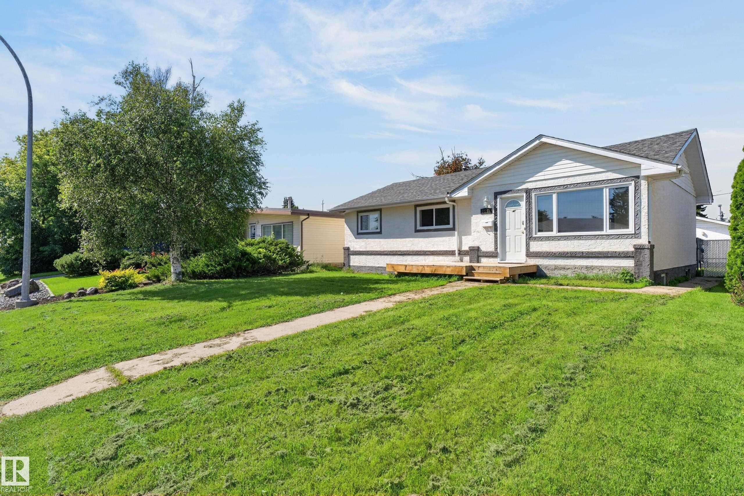 White exterior with textured dark grey trim, white framed windows, and a wood-toned front deck - 13214 123 Street Nw, Edmonton, AB