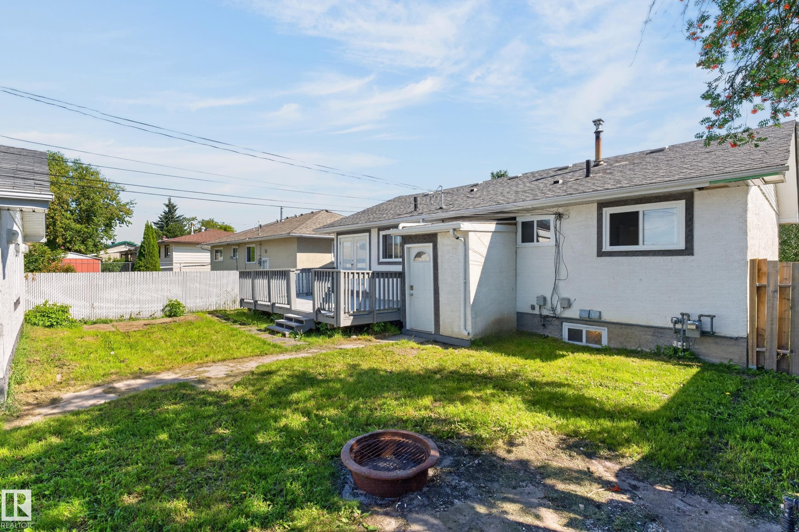 Spacious backyard with a grey wood deck, white vinyl fencing, and a separate side entrance - 13214 123 Street Nw, Edmonton, AB