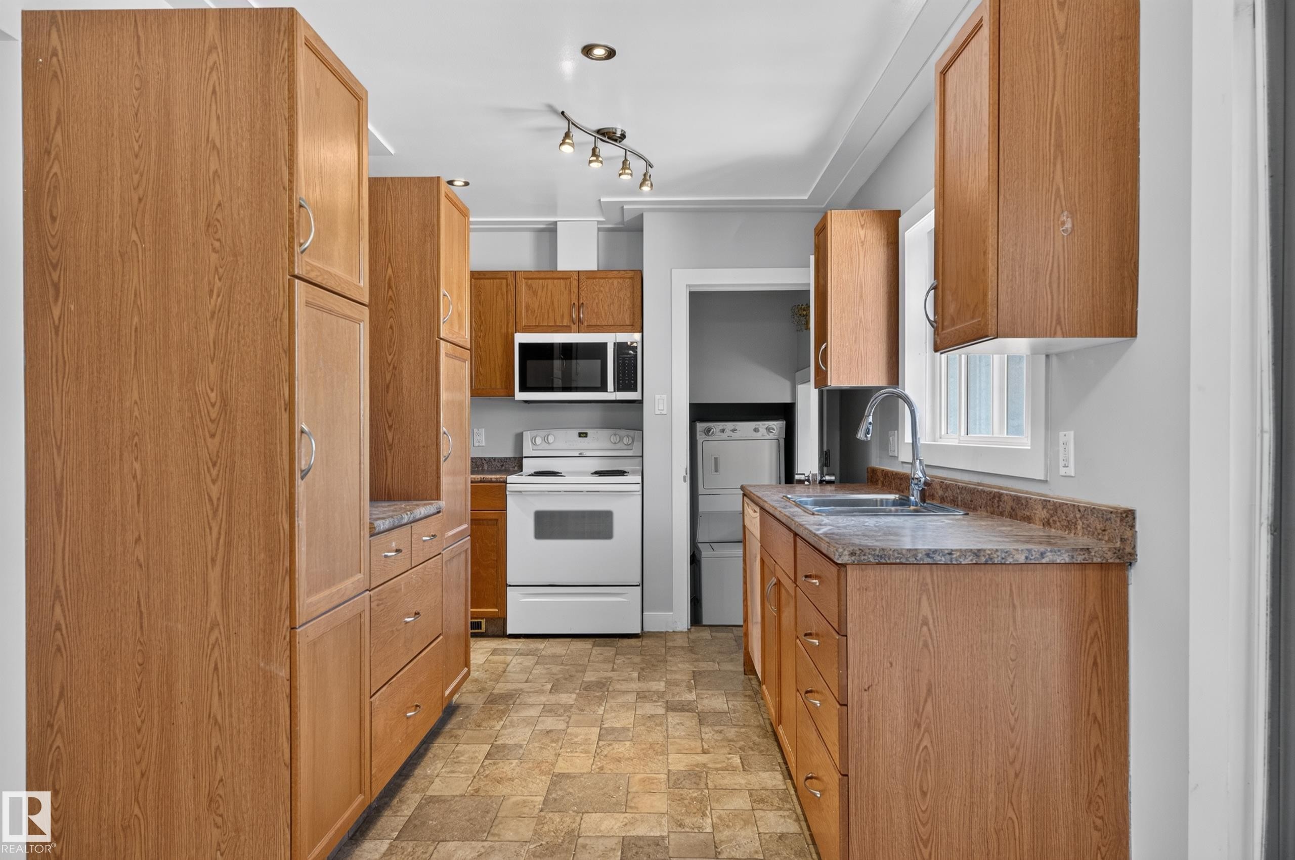 Galley kitchen featuring wood-finish cabinetry, patterned flooring, white appliances, and track lighting - 13214 123 Street Nw, Edmonton, AB