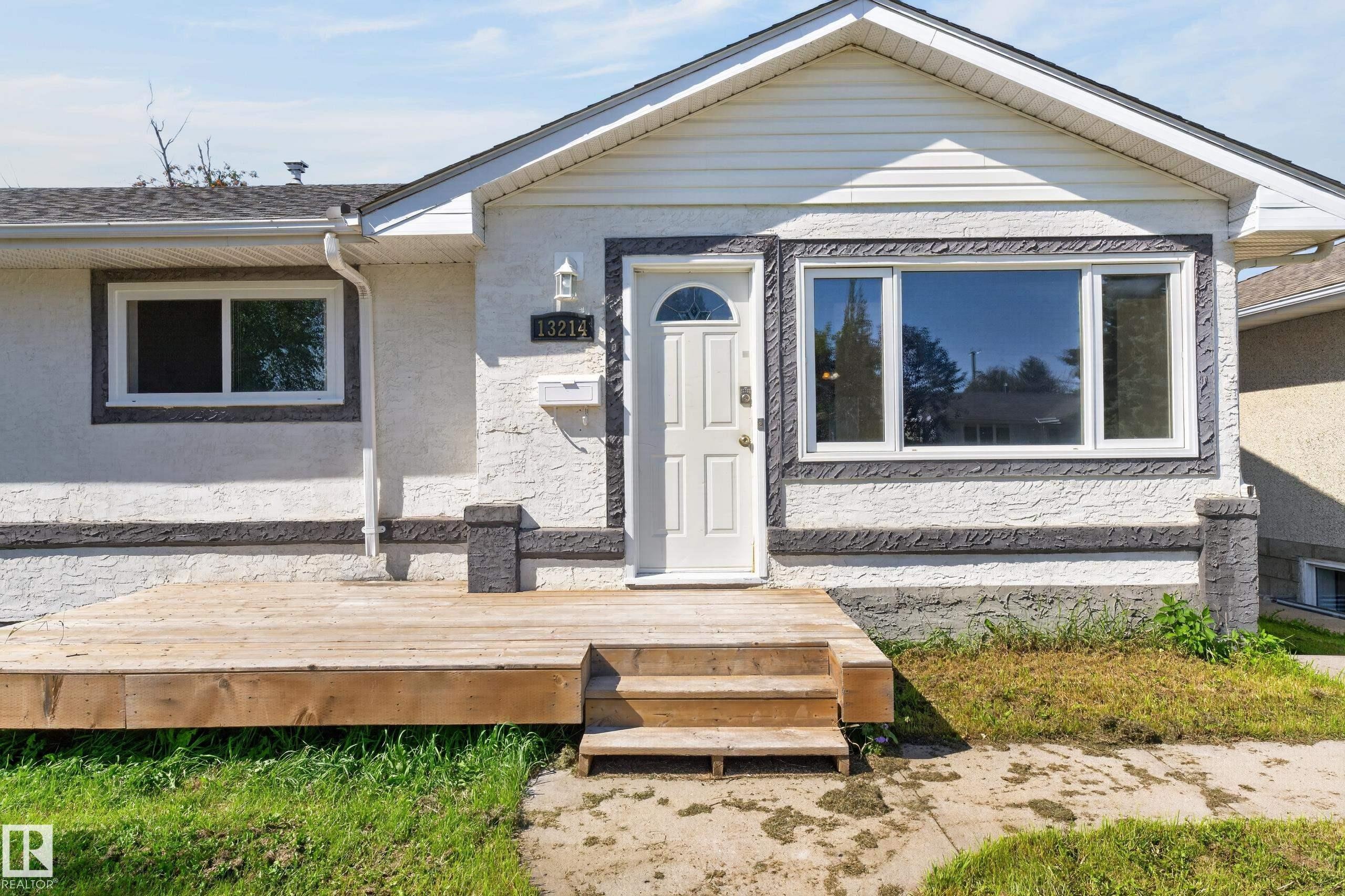 White stucco exterior with dark textured trim accents, front wood deck with steps, prominent front door with arched glass insert, and multiple windows - 13214 123 Street Nw, Edmonton, AB