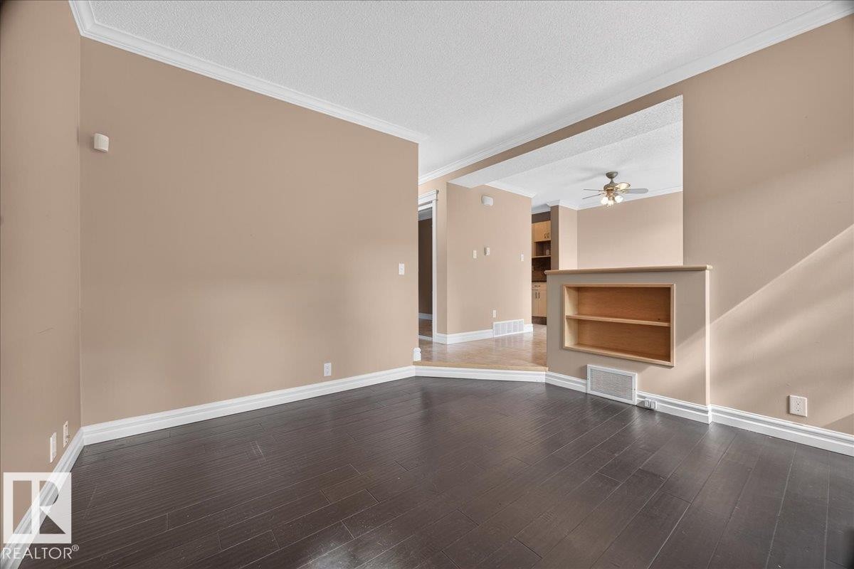 Dark wood-finish flooring with white trim, recessed built-in shelving, and a dropped ceiling with crown molding - #47 3812 20 Av Nw, Edmonton, AB