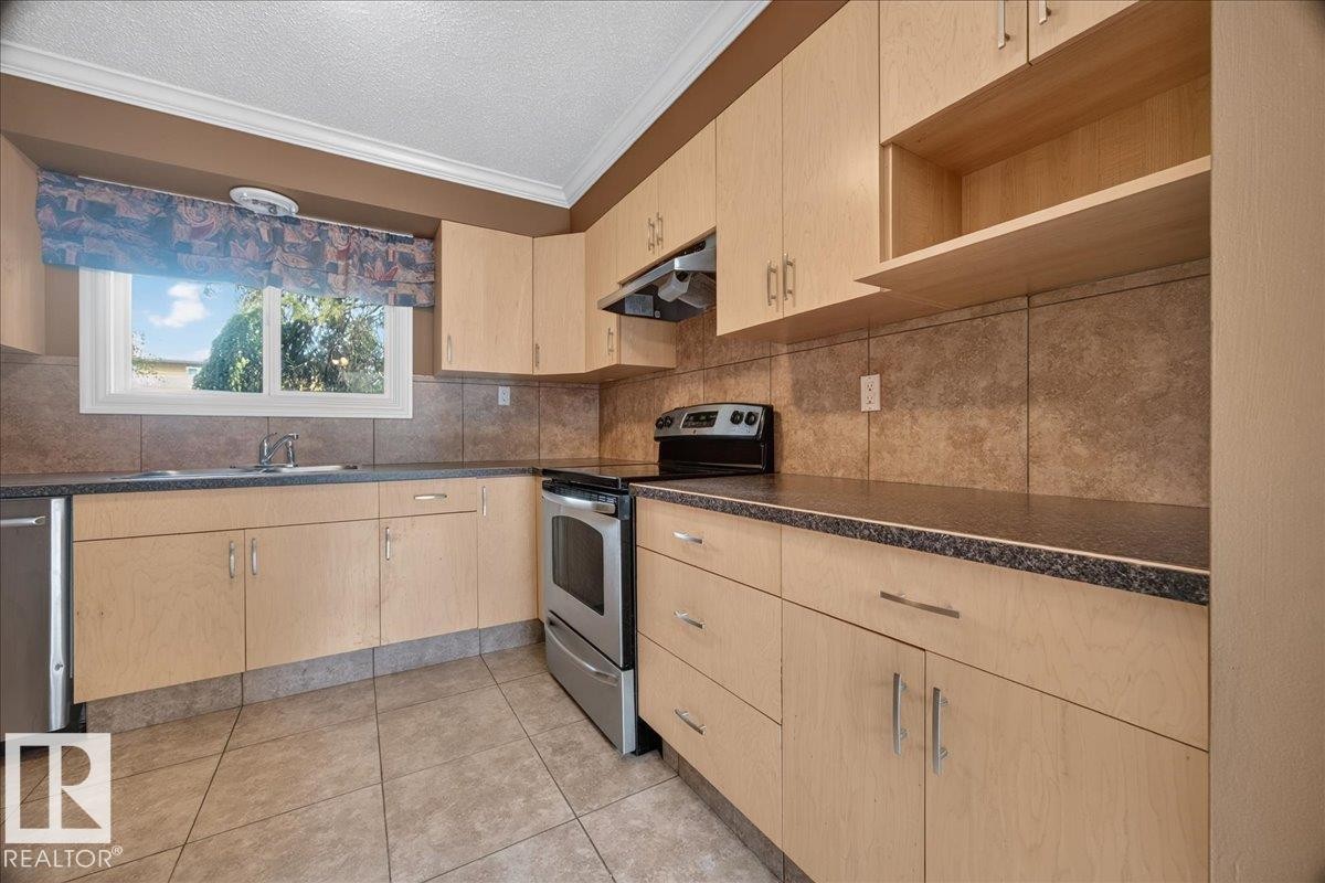 Kitchen with light wood-finish cabinetry, stainless steel appliances, speckled dark countertops, and a tiled backsplash - #47 3812 20 Av Nw, Edmonton, AB
