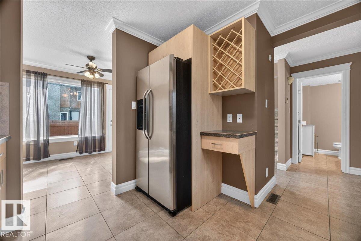 Tile flooring, stainless steel refrigerator, built-in wine rack, integrated desk area with drawer, and crown molding - #47 3812 20 Av Nw, Edmonton, AB