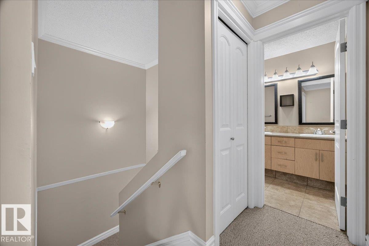 Carpeted staircase with white handrail, leading to a bathroom featuring a dual vanity with light wood-finish cabinetry, two framed mirrors, and tile flooring - #47 3812 20 Av Nw, Edmonton, AB