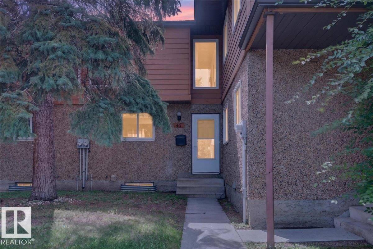 Two-story exterior with textured siding, accent wood-finish siding, white framed windows, and a concrete walkway - #47 3812 20 Av Nw, Edmonton, AB