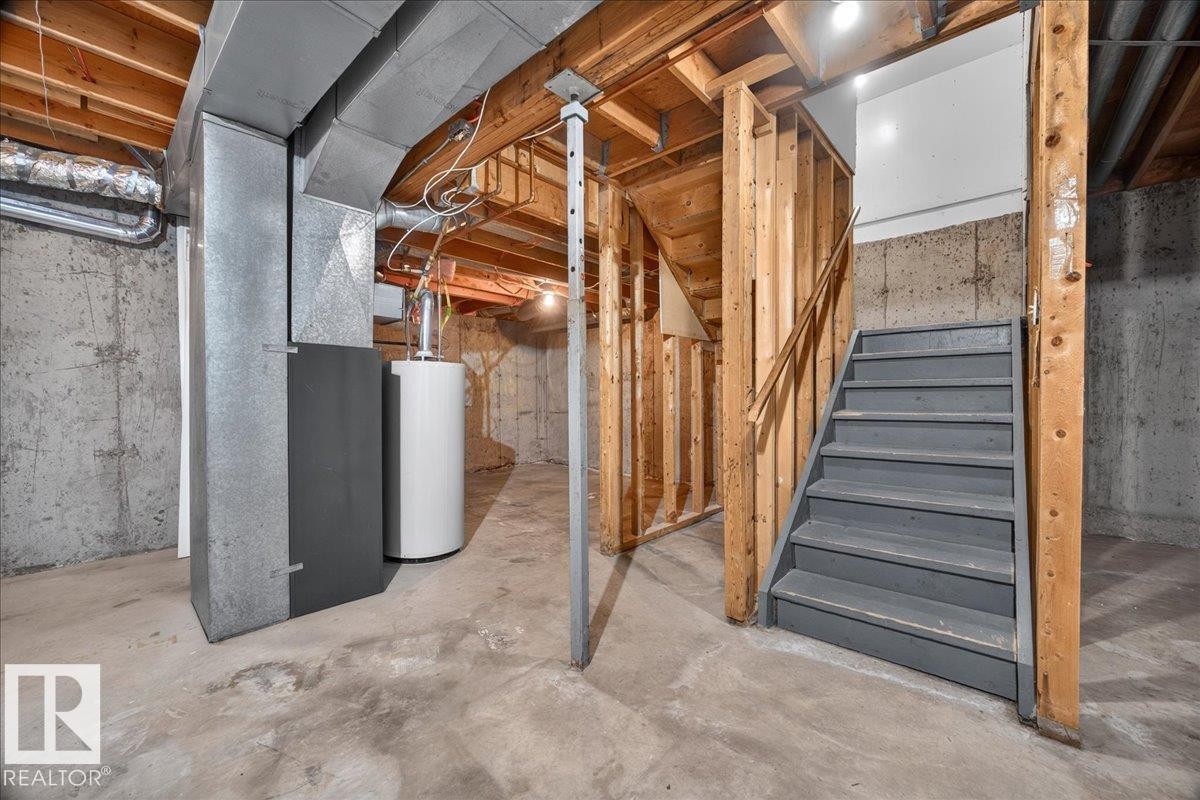 Concrete flooring, exposed ceiling joists, wood-framed unfinished walls, built-in staircase with painted treads, and visible ductwork - #47 3812 20 Av Nw, Edmonton, AB