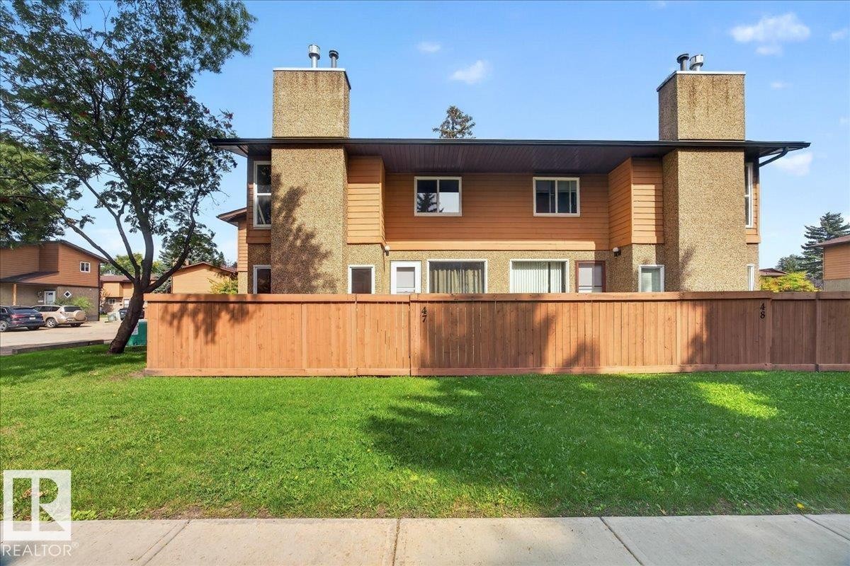 Modern multi-level residence featuring a distinctive architectural design with stacked stone chimney elements, warm-toned exterior siding, and horizontal wood-finish fencing - #47 3812 20 Av Nw, Edmonton, AB