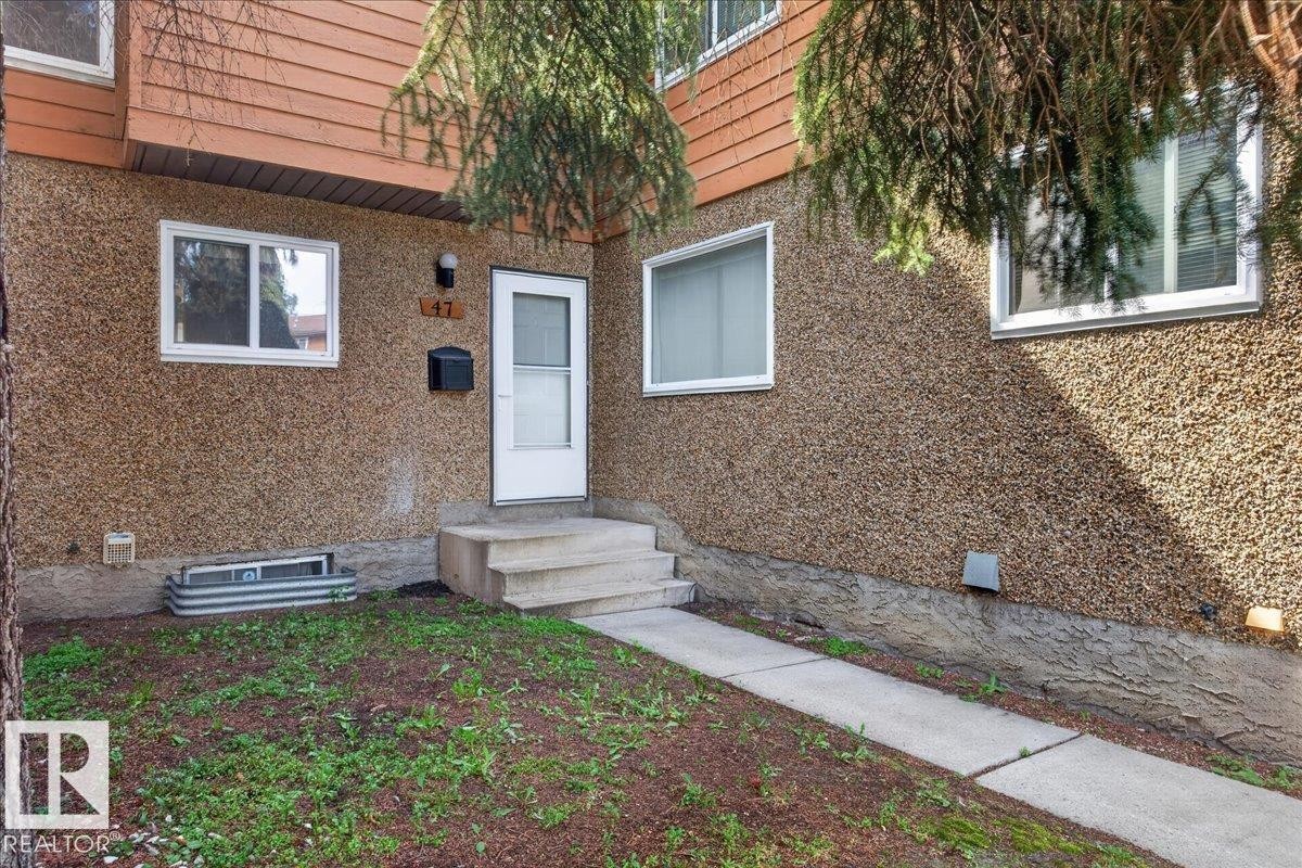 Stucco exterior with upper-level wood paneling, front entry door with glass insert, concrete walkway, and exterior lighting - #47 3812 20 Av Nw, Edmonton, AB