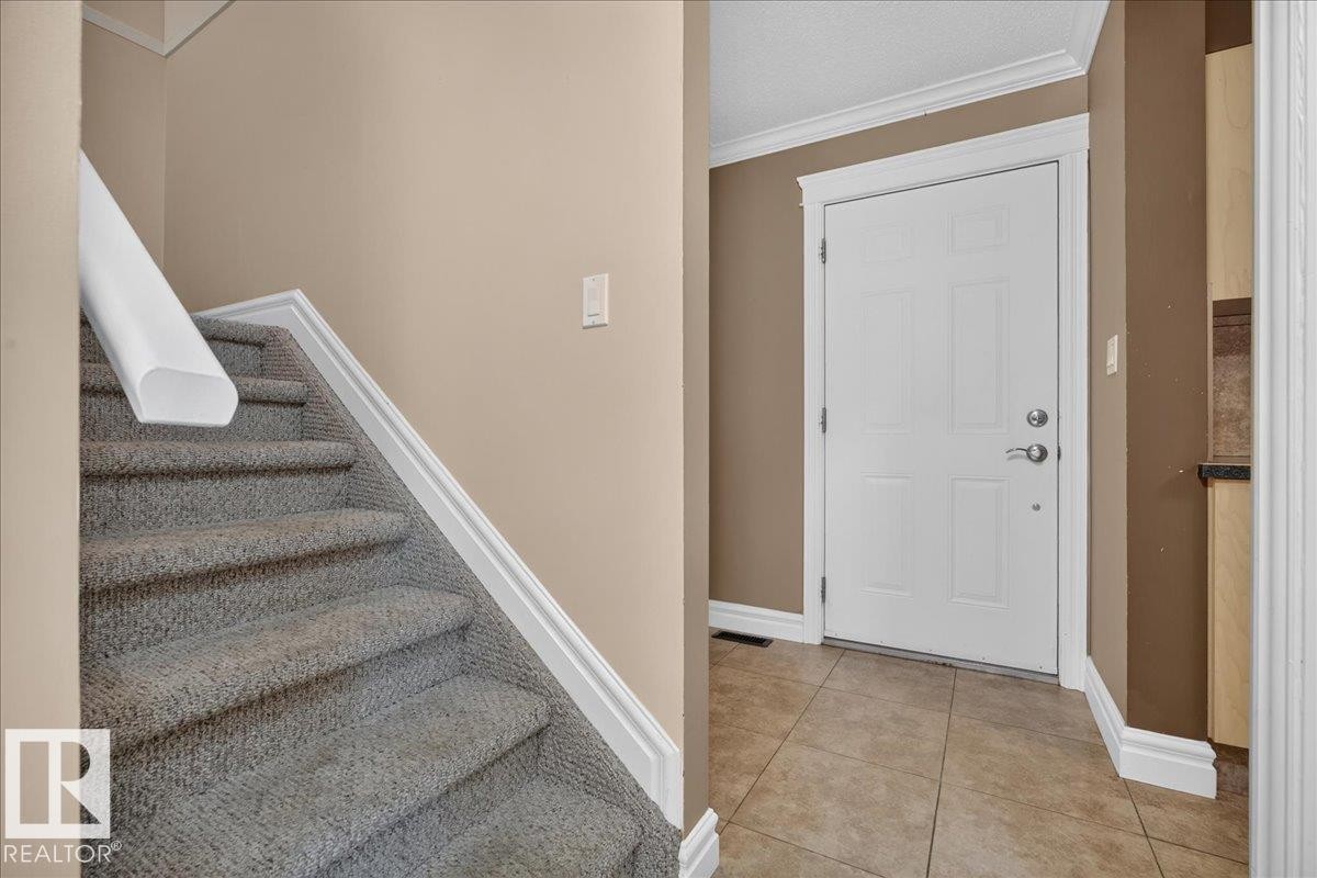 Carpeted staircase, tiled entry flooring, white panel door, and white trim accents - #47 3812 20 Av Nw, Edmonton, AB