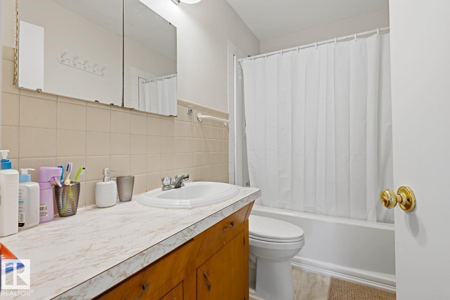 Bright bathroom featuring a wood-finish vanity with marble-look countertop, white subway tile backsplash, and mirrored medicine cabinet - 9740 63 Avenue Nw, Edmonton, AB