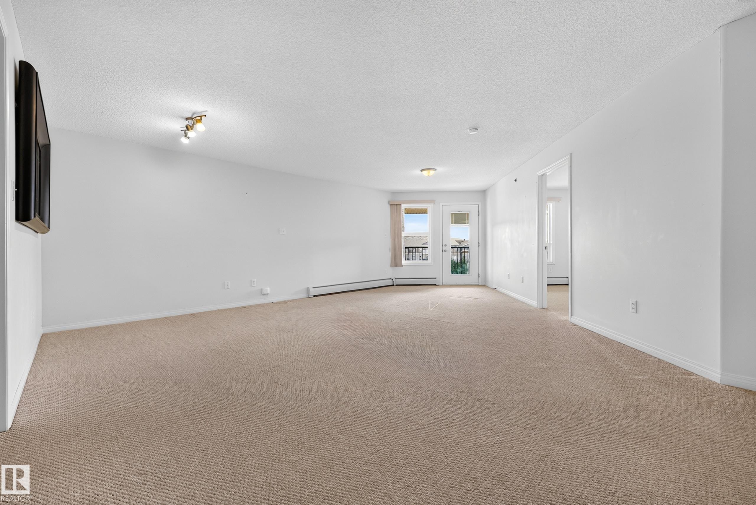 Spacious living area featuring neutral carpet flooring, recessed ceiling lighting, and glass sliding doors with access to a covered balcony - #6430 7331 South Terwillegar Dr Nw, Edmonton, AB